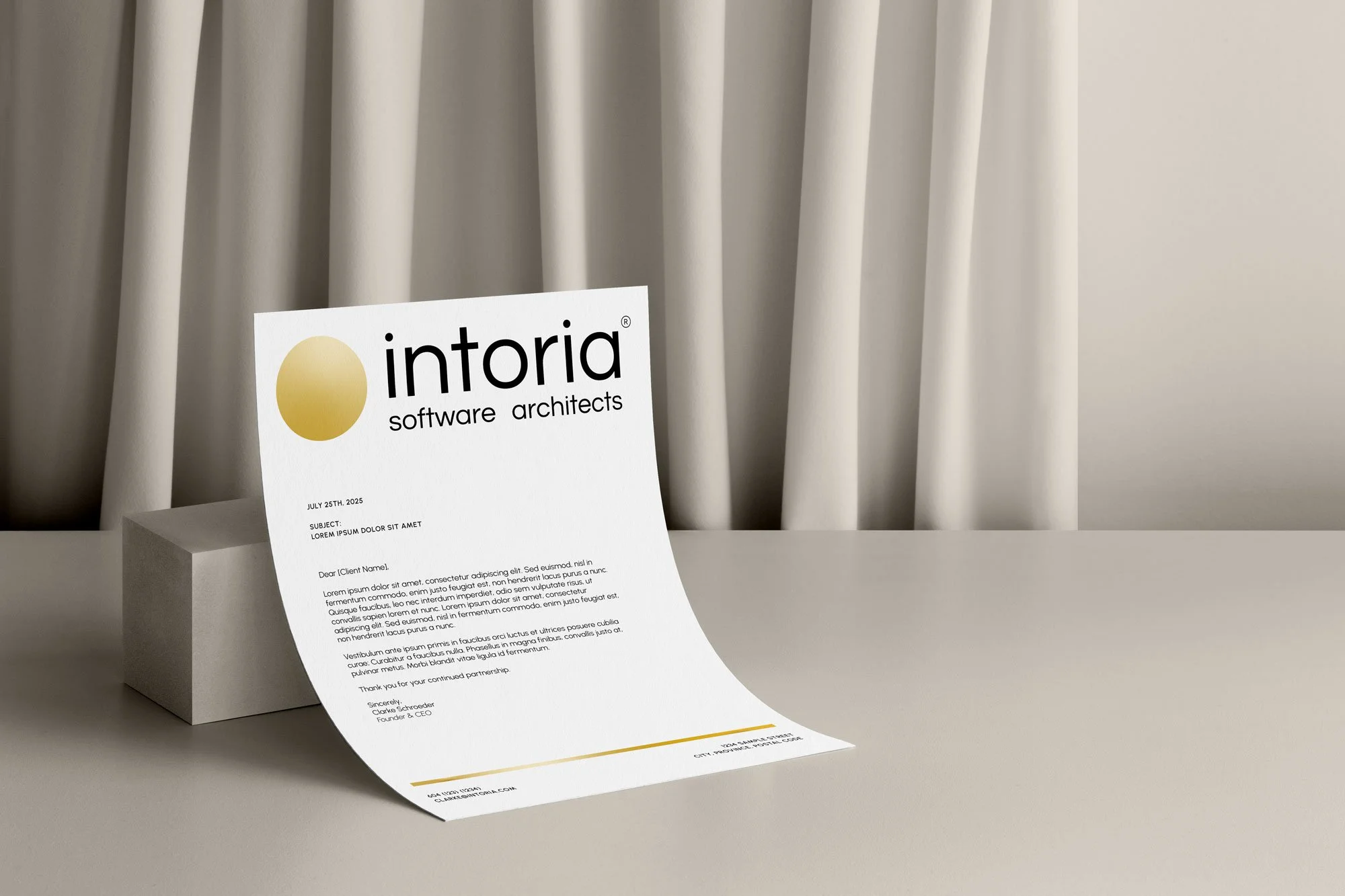 A white sheet of paper with business letter content placed on a white table, with a white curtain background, showing a logo with a gold circle and the text 'intoria software architects'.
