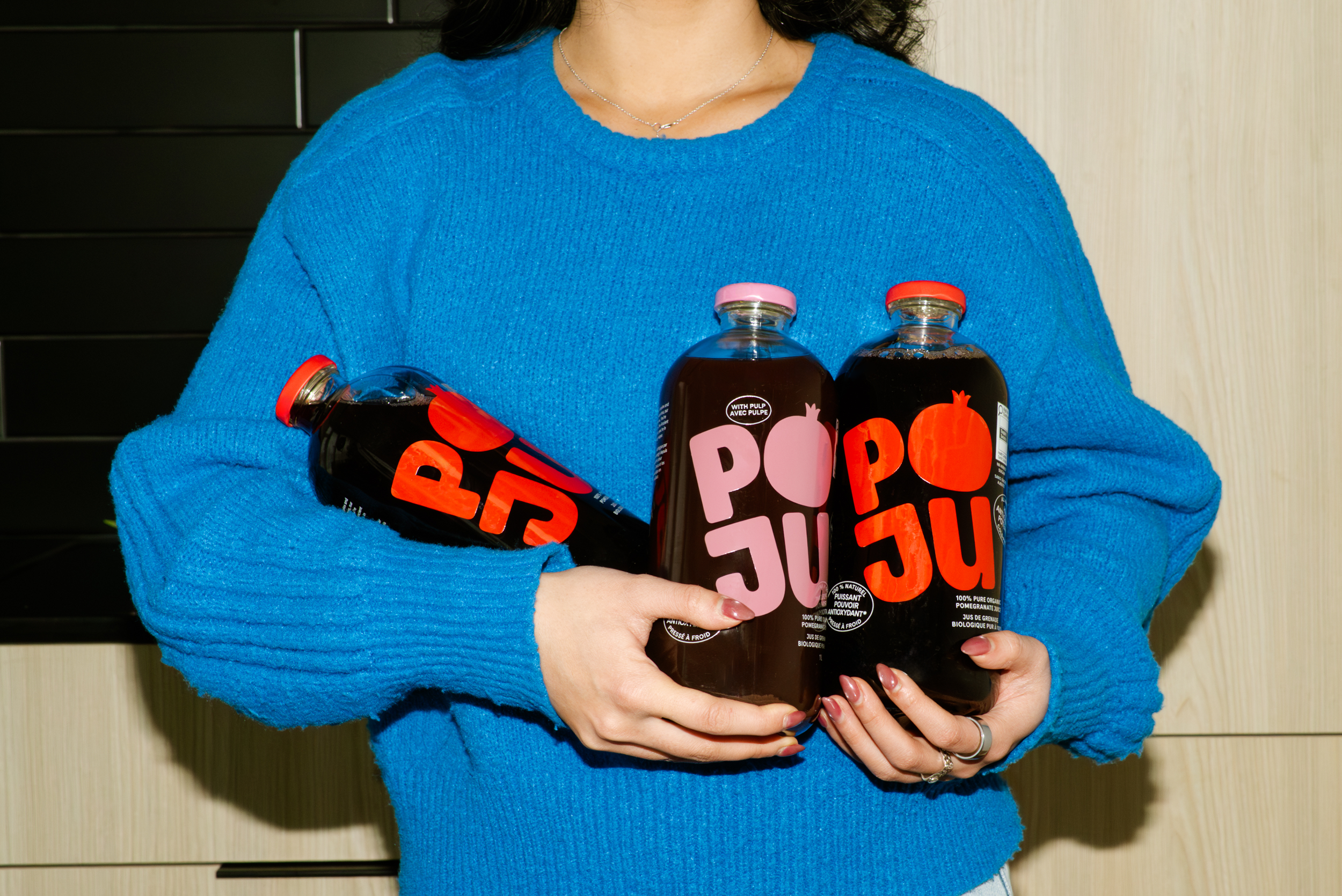 Person wearing a blue sweater holding three bottles of pomegranate juice with red and pink caps.
