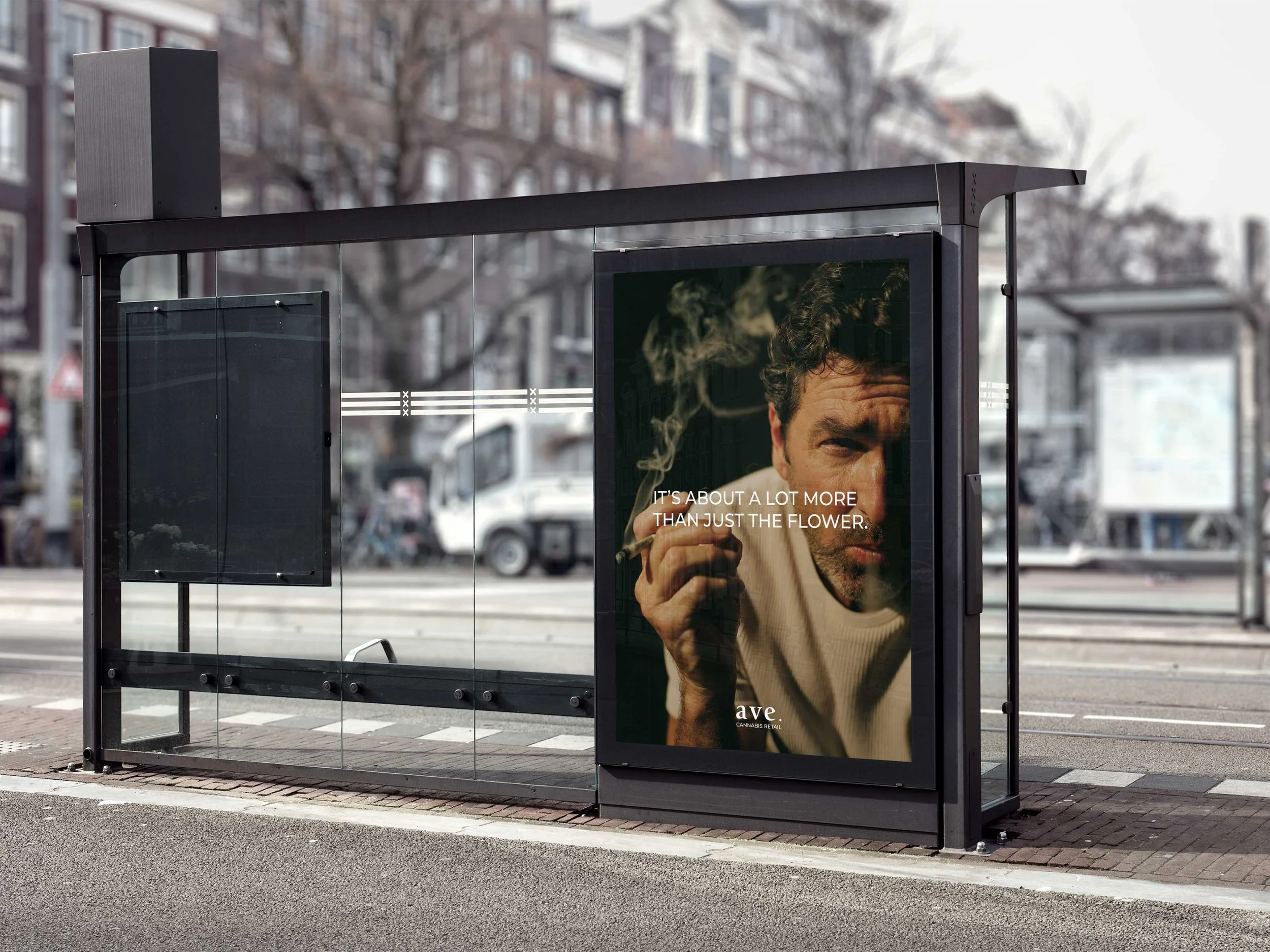 Bus stop shelter with large advertisement featuring a man smoking and a quote, located on a city street with apartment buildings in the background.