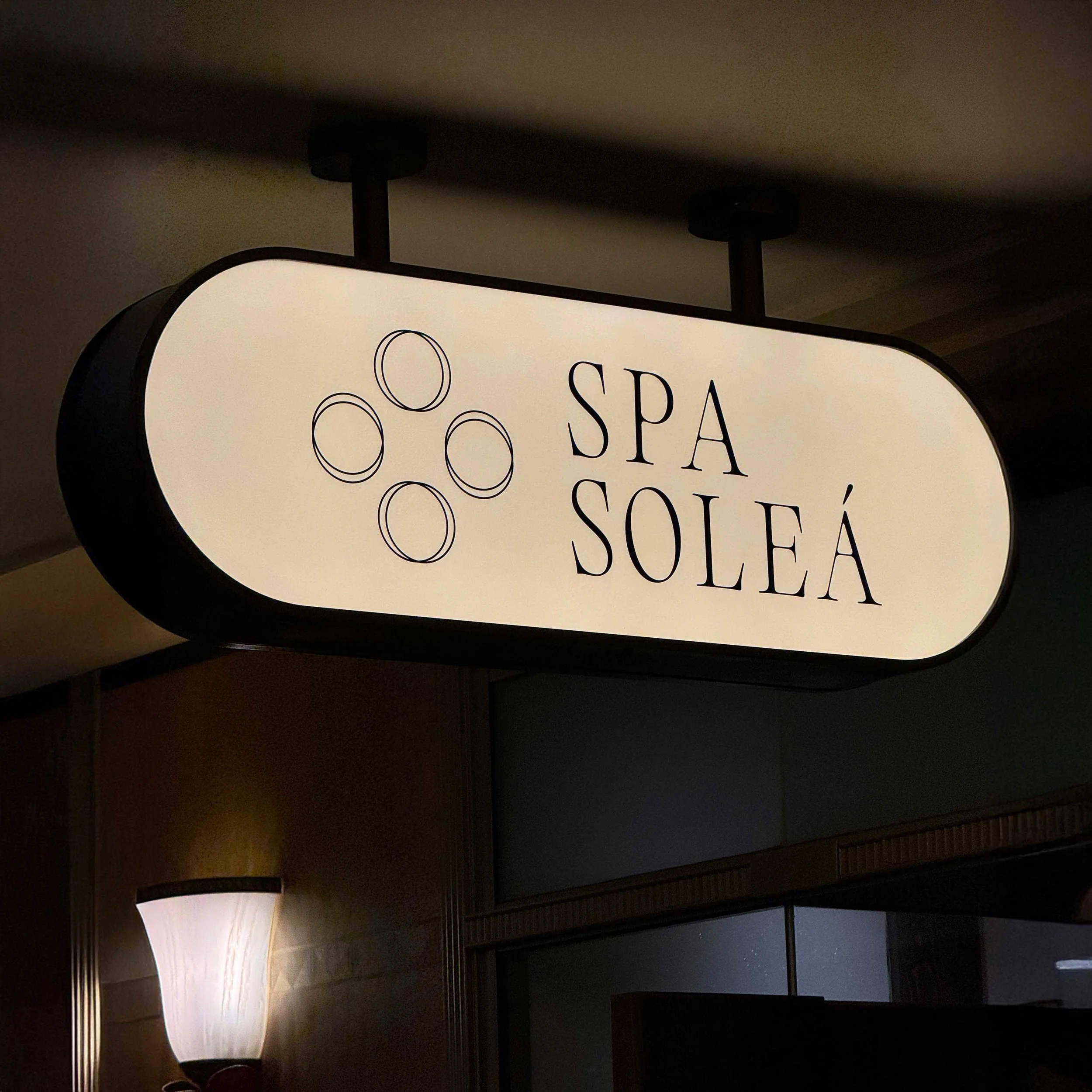 A photo of a sign with the text 'Spa Solea' and a decorative element, taken indoors with a ceiling and light fixtures visible above.