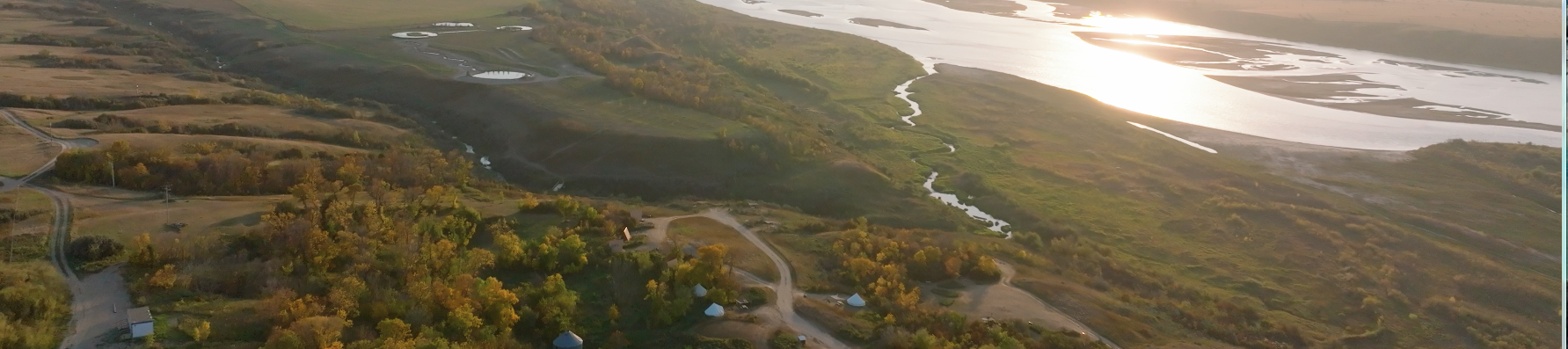 Aerial view of a landscape with water bodies, green fields, and trees during sunset.