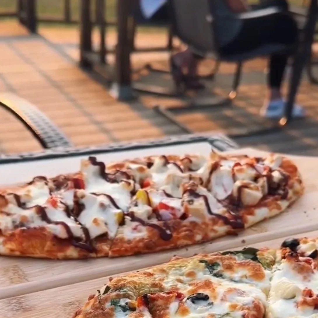 Two pizzas on a wooden serving board, outdoors on a patio.