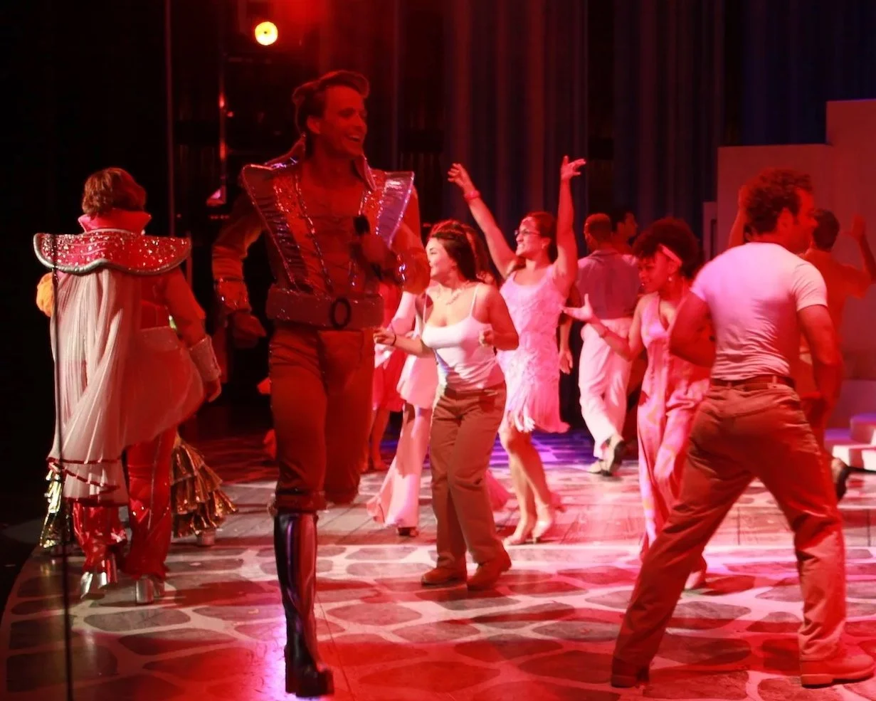 People dancing on stage with red lighting in a theatrical performance.