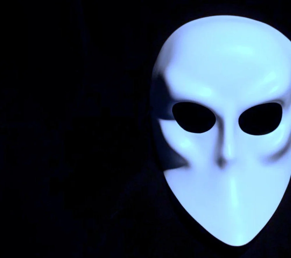 A white skull-shaped mask with black eye holes on a black background.