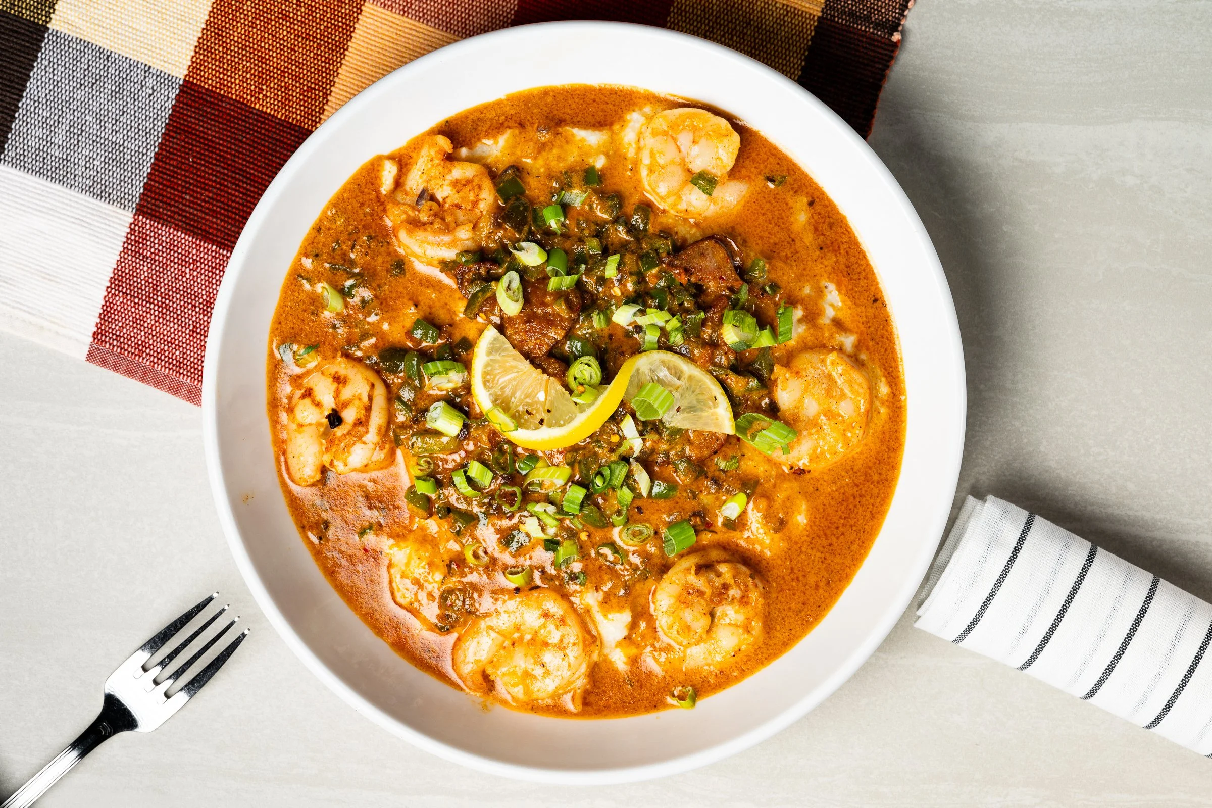 Bowl of richly seasoned soup or stew garnished with fresh herbs and lime.