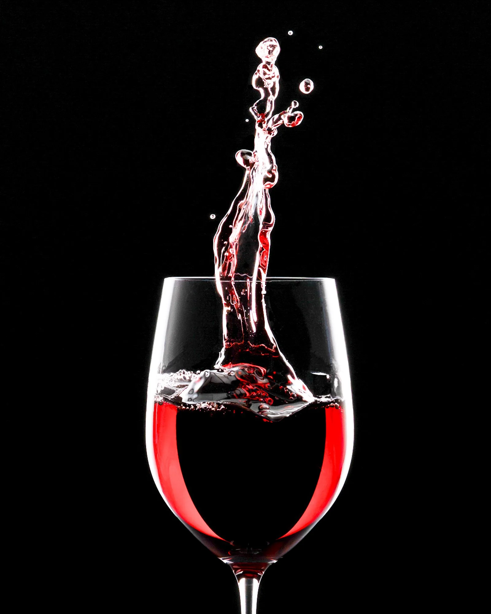 Red beverage splashing into a wine glass against a black background.