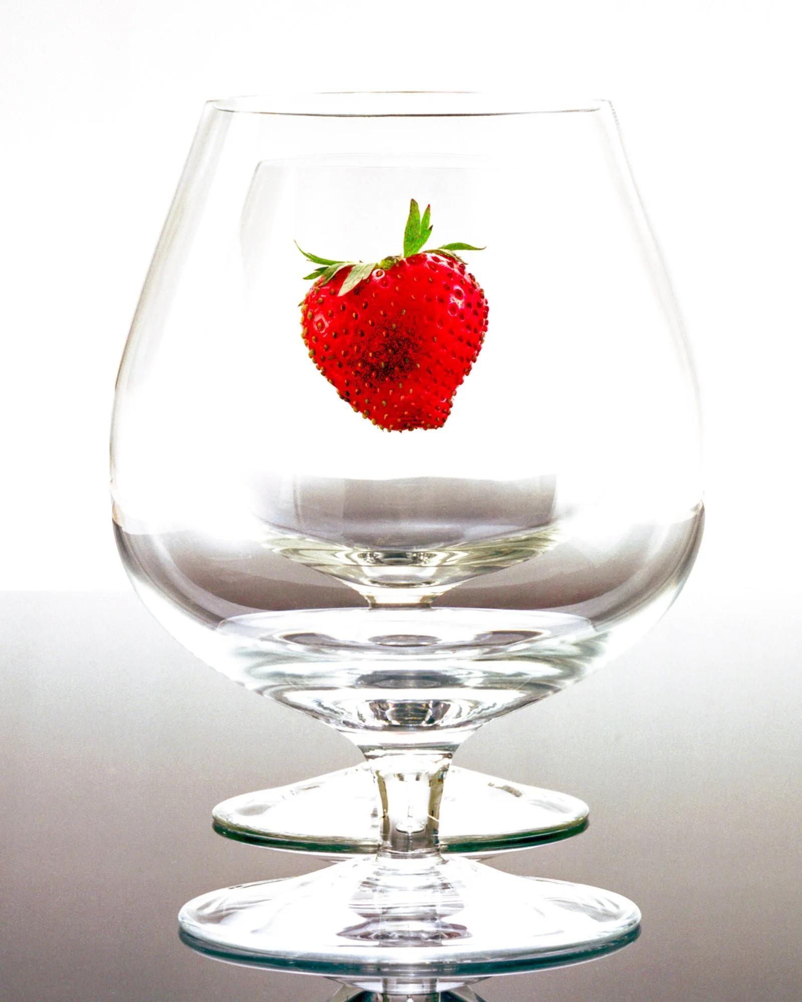 Fresh strawberry suspended above or inside a clear drinking glass.