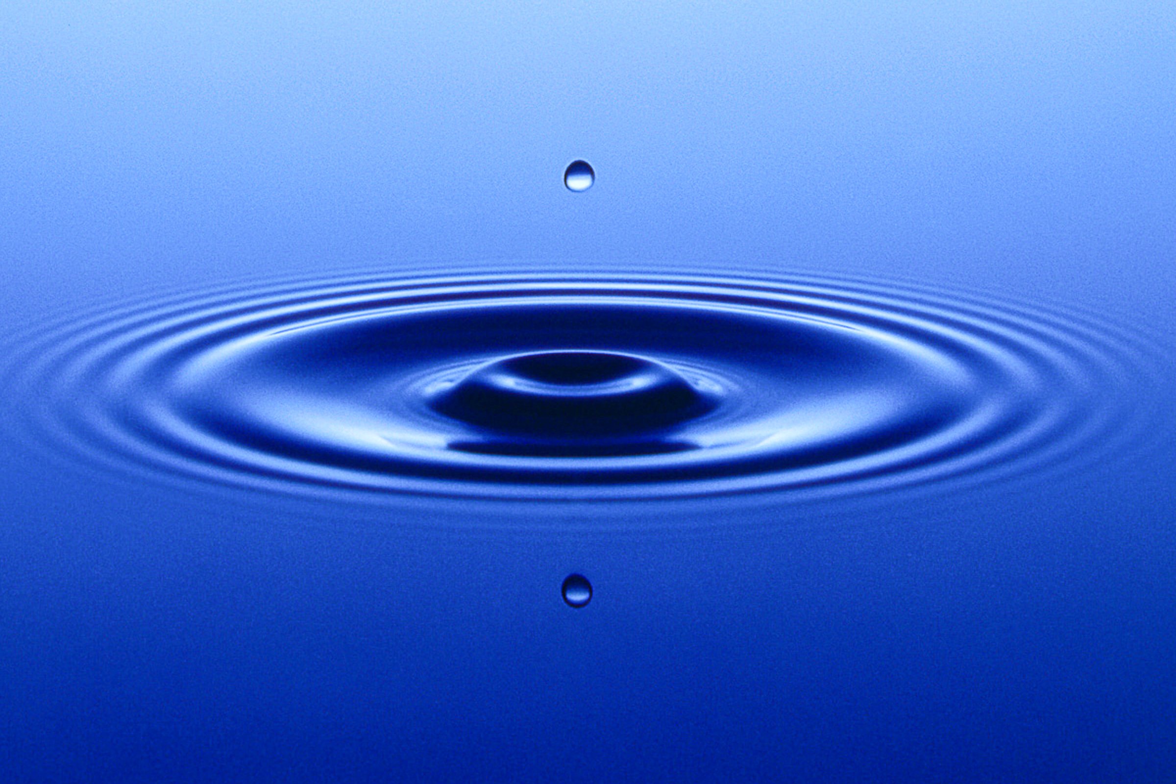 Blue water droplet creating concentric ripples in a clean conceptual image.