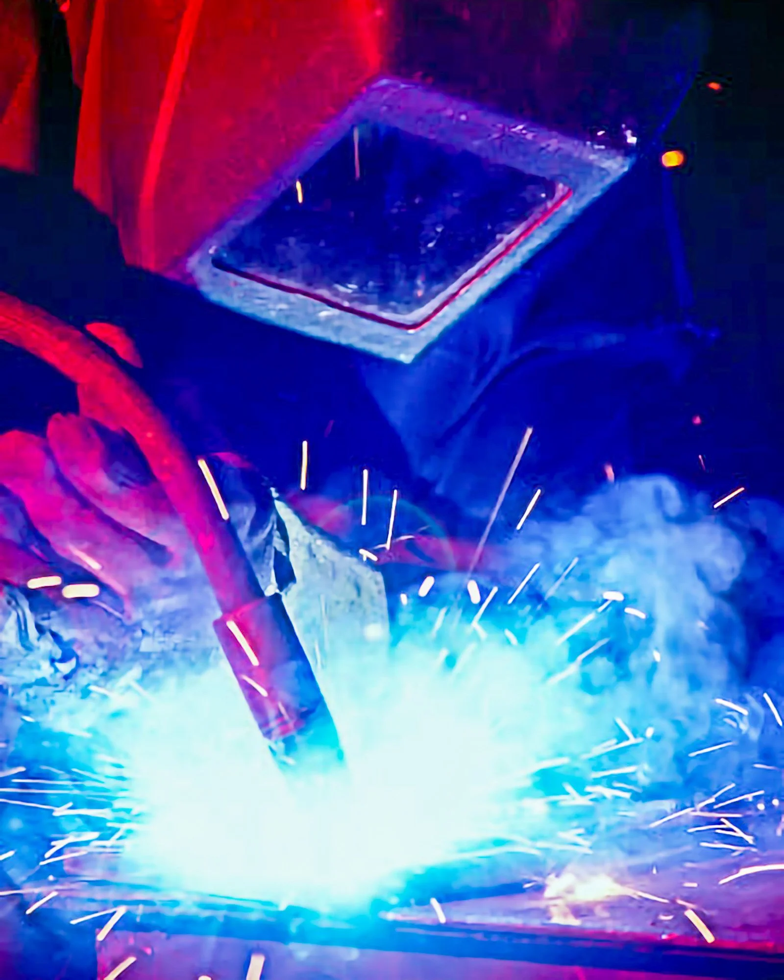 Industrial welding process photographed with bright sparks and blue light.