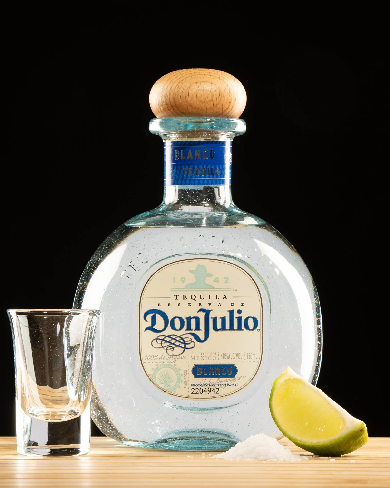 Don Julio tequila bottle with shot glass and lime against a dark background.