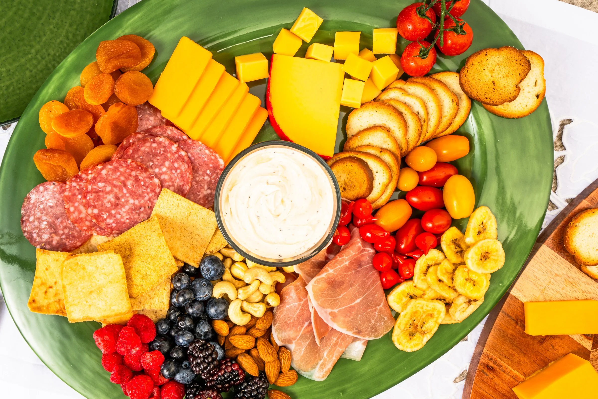 Charcuterie board arranged with cheeses, cured meats, crackers, nuts, fruits, and vegetables.