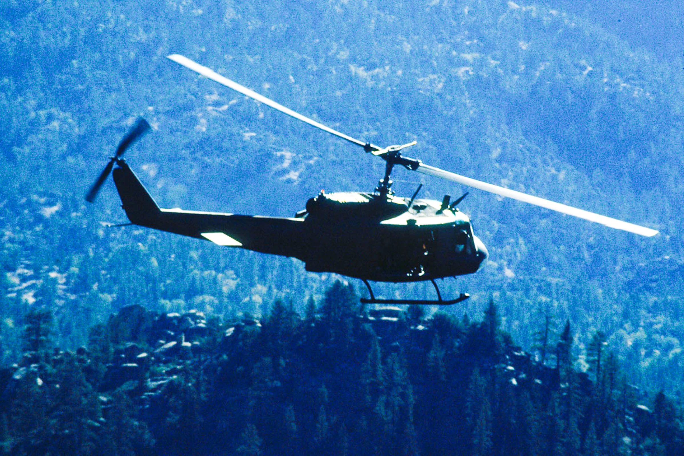 Helicopter photographed in flight against tree lined mountains