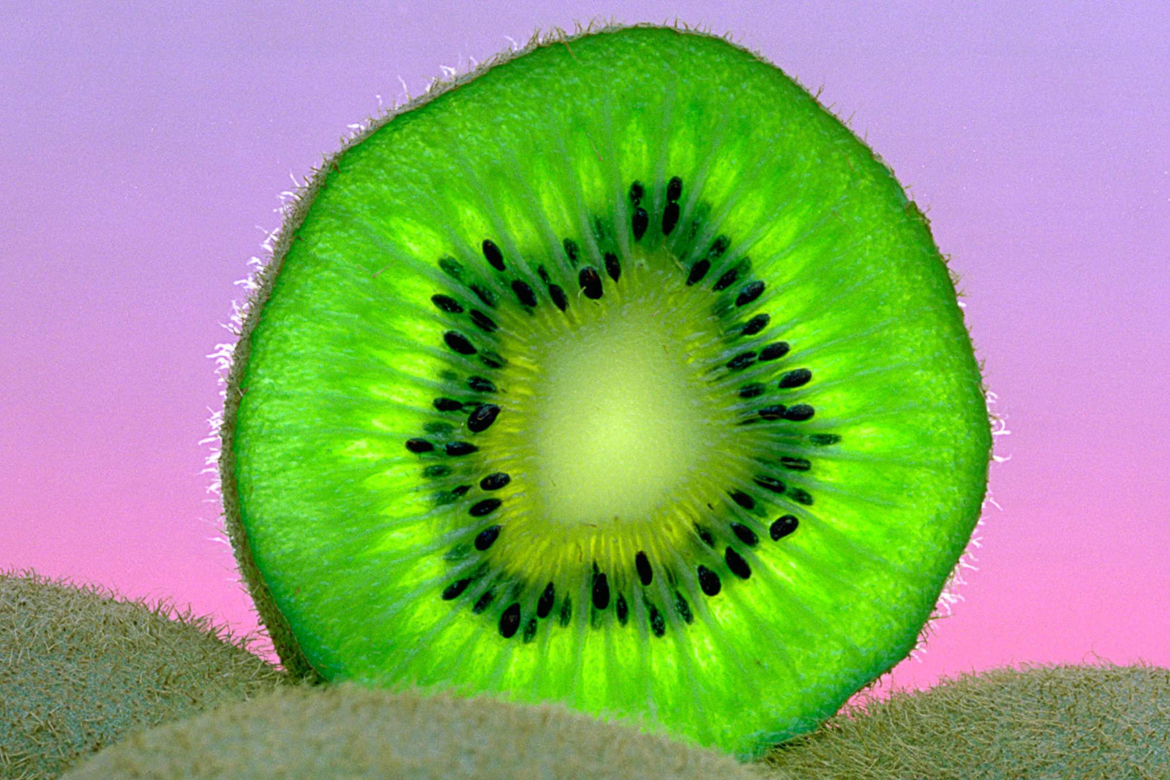 Close-up cross section of a fresh kiwi fruit against a colorful background.