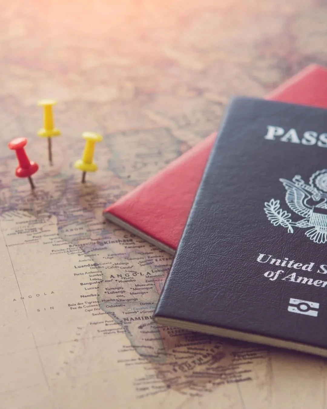 U.S. passport and a small red notebook on a world map, with three yellow and one red pushpins.