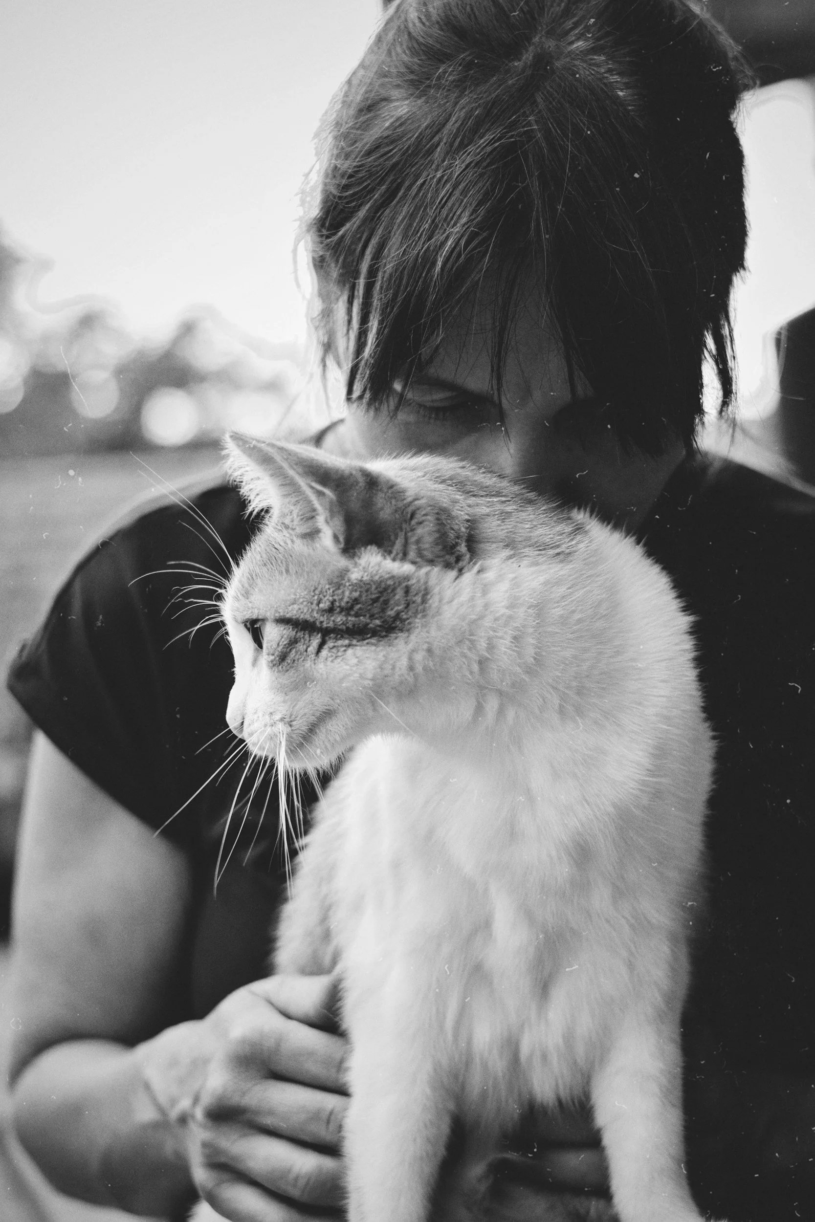 A person holding a cat, in black and white. The person has dark hair and is looking down, with the cat close to their face.