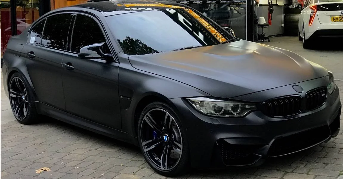 Black BMW sedan parked outside in front of a garage with dark tinted windows.