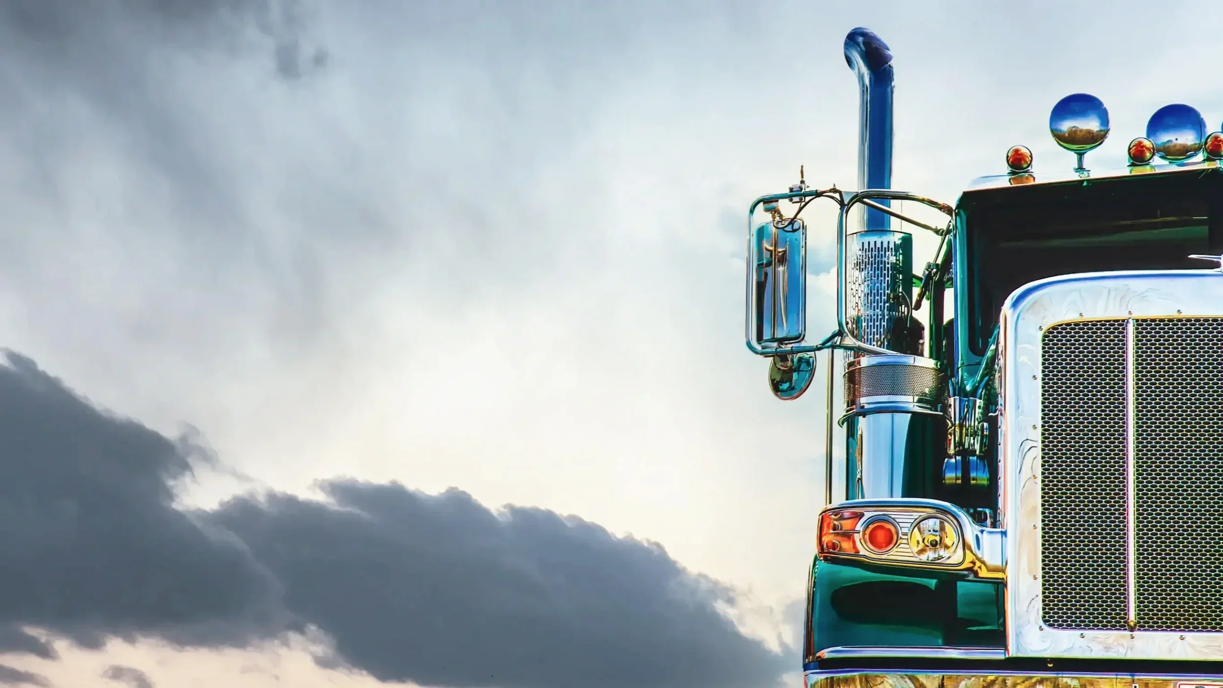 Close-up of the front of a shiny, green semi-truck cab against a cloudy sky.
