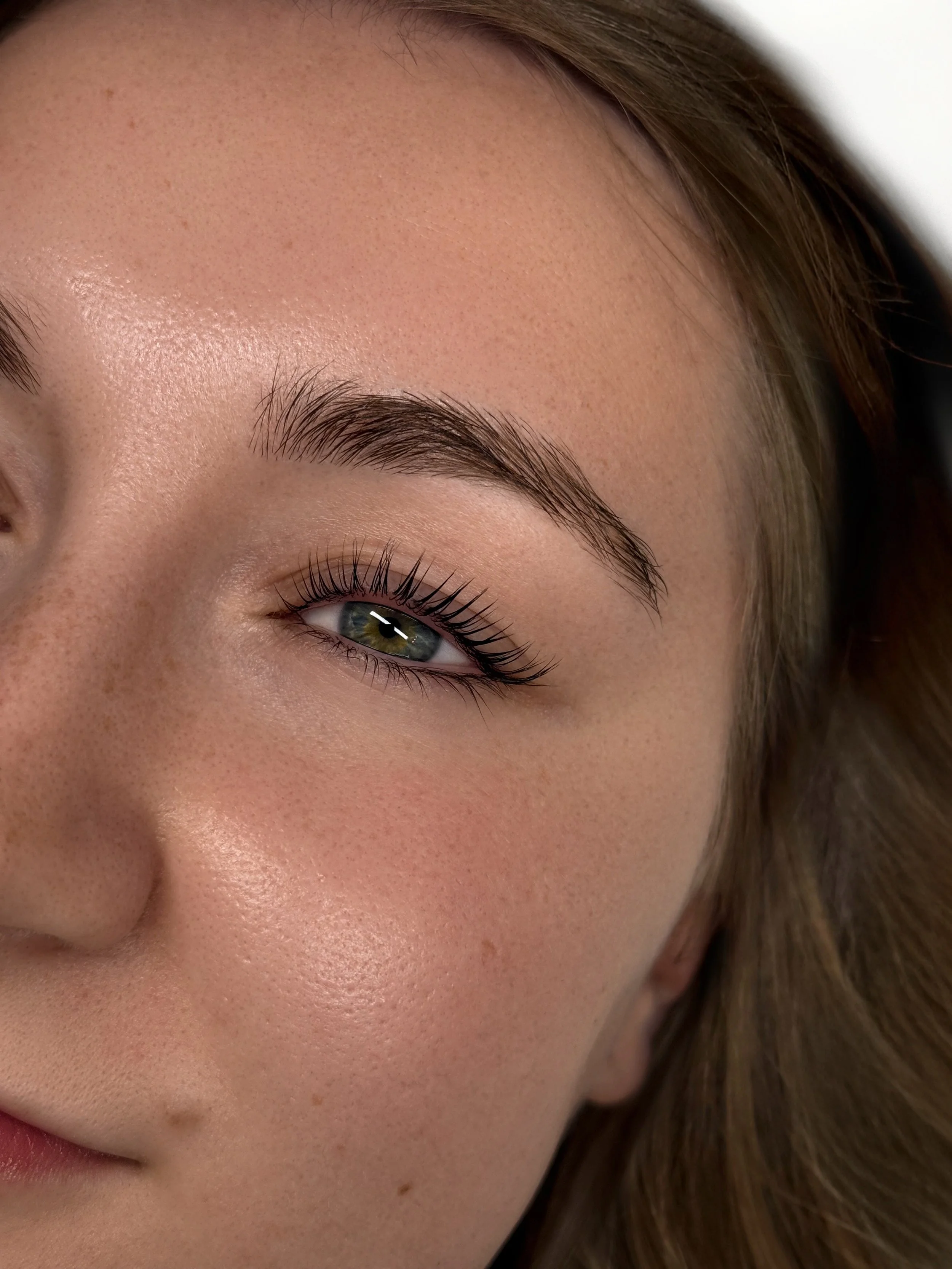 Close-up of a woman's face showing her eye, eyebrow, and part of her cheek and nose, with smooth skin, long eyelashes, and light makeup.