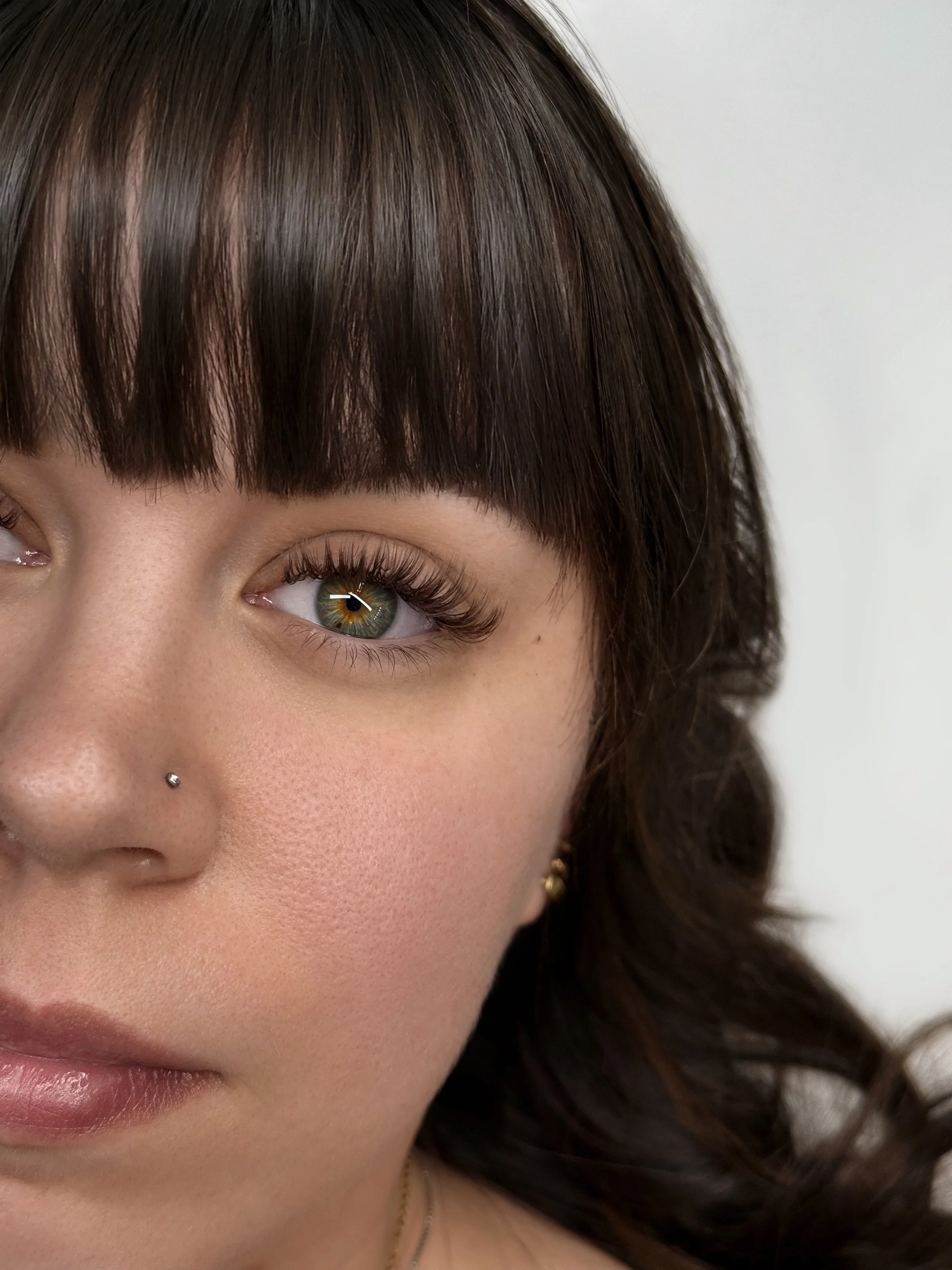 Close-up portrait of a young woman with brown hair, green eyes, and a nose piercing, looking to the right.