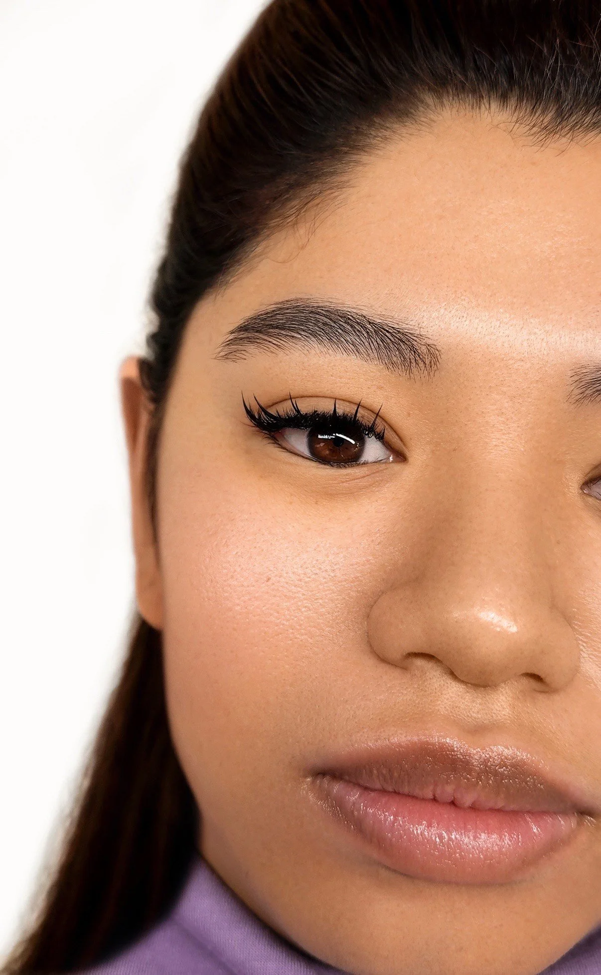 Close-up of a woman's face showing her eye, eyebrow, nose, and lips, with a neutral background.