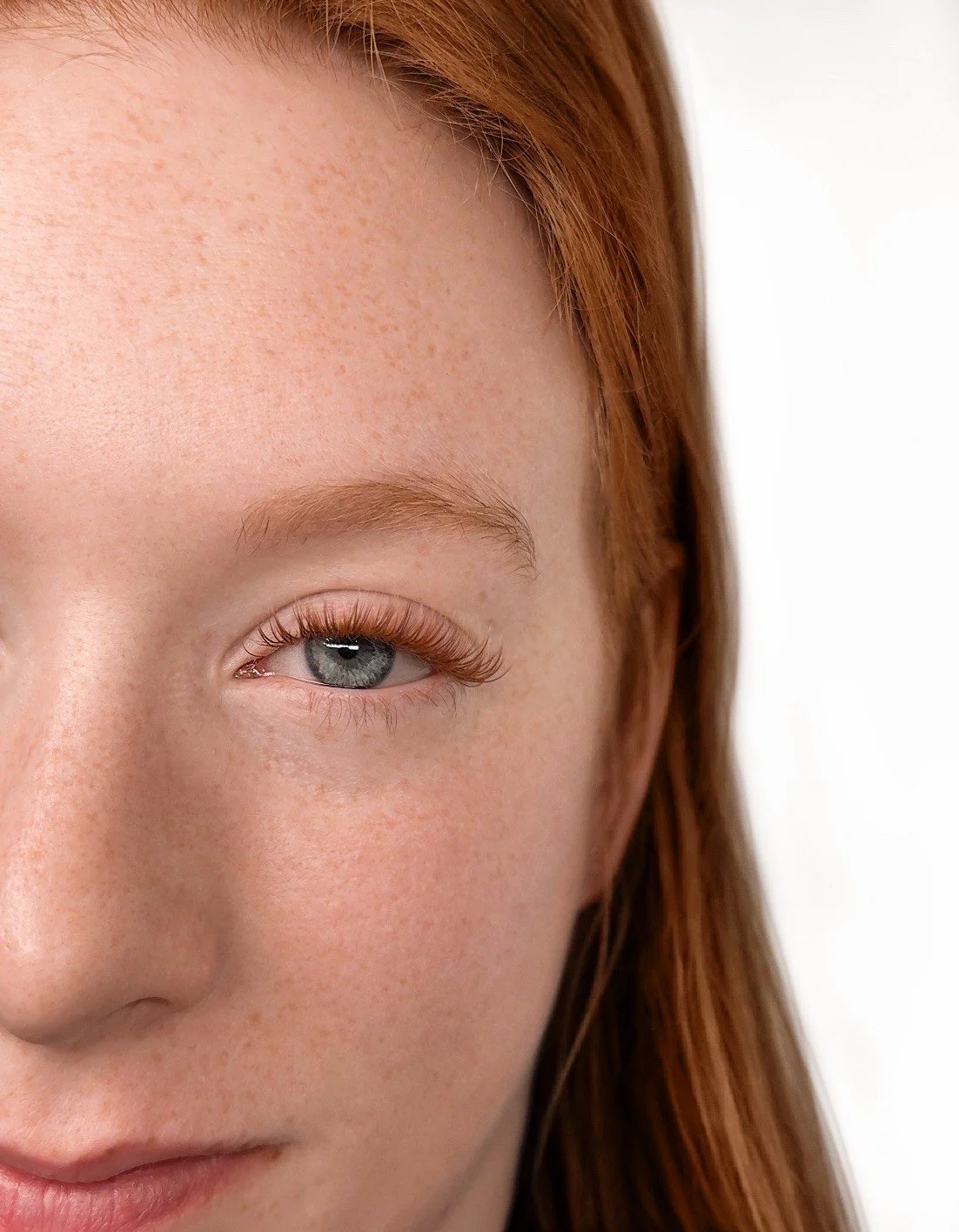 Close-up of a woman's face showing her eye with light makeup, freckles, and red hair.