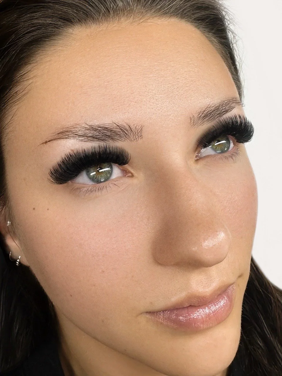 Close-up of a woman with fair skin, gray eyes, and long black eyelash extensions, looking slightly upward.