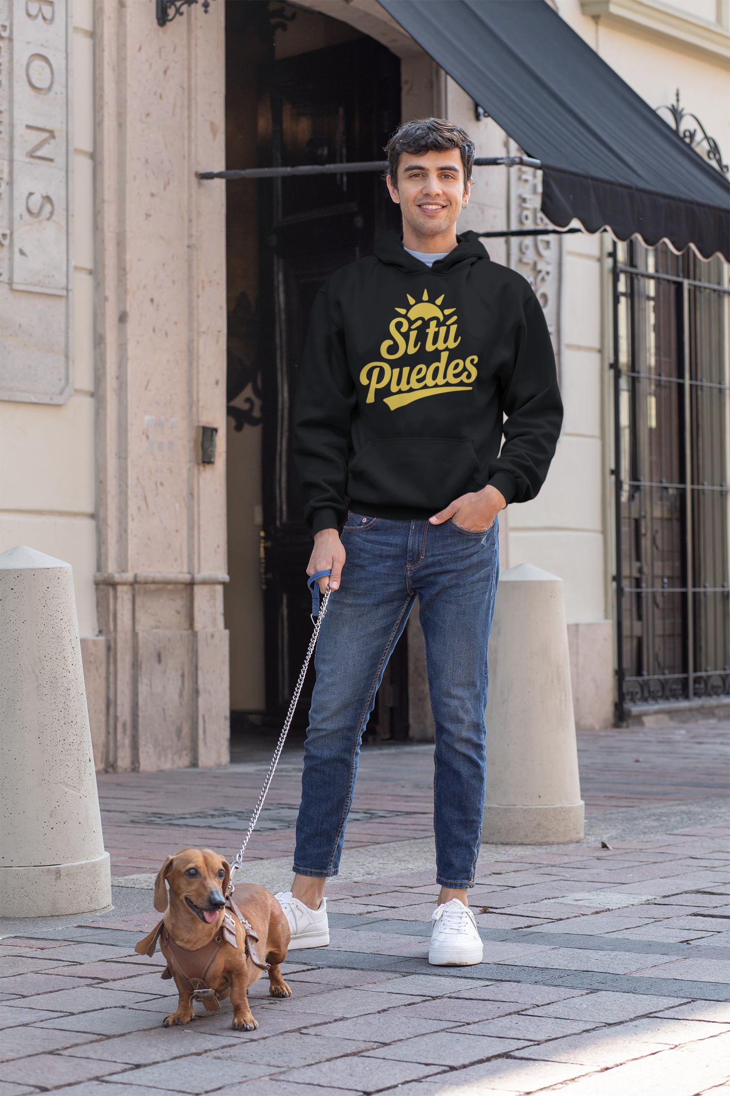 Young man walking his dog in city wearing black ‘Sí Tú Puedes’ motivational hoodie with yellow text — E.N.K. Feel Good Apparel streetwear