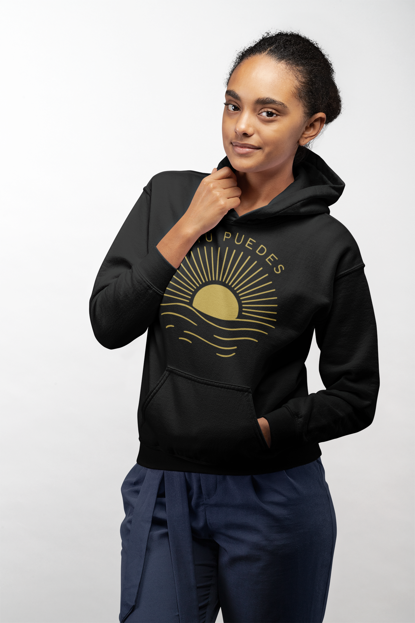 Young woman in black ‘Sí Tú Puedes’ hoodie with sun and waves graphic, casual motivational streetwear — E.N.K. Feel Good Apparel