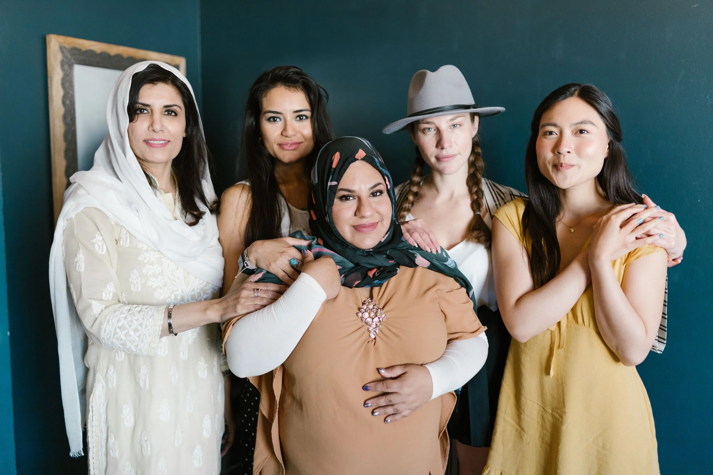 5 women standing together in front of a dark teal-blue background.