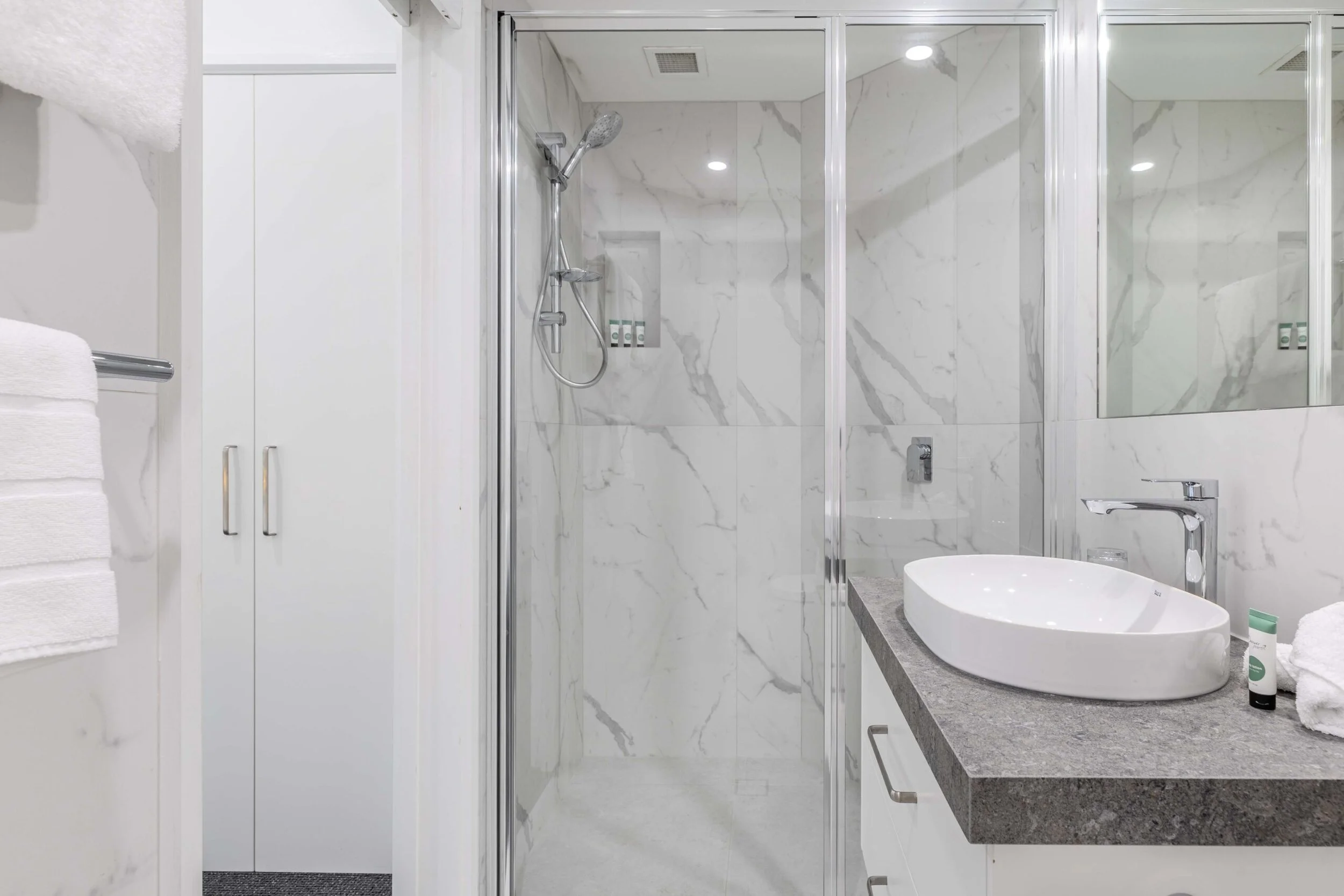 Modern bathroom with a glass shower enclosure, marble tiles, a countertop with a vessel sink, and towels.