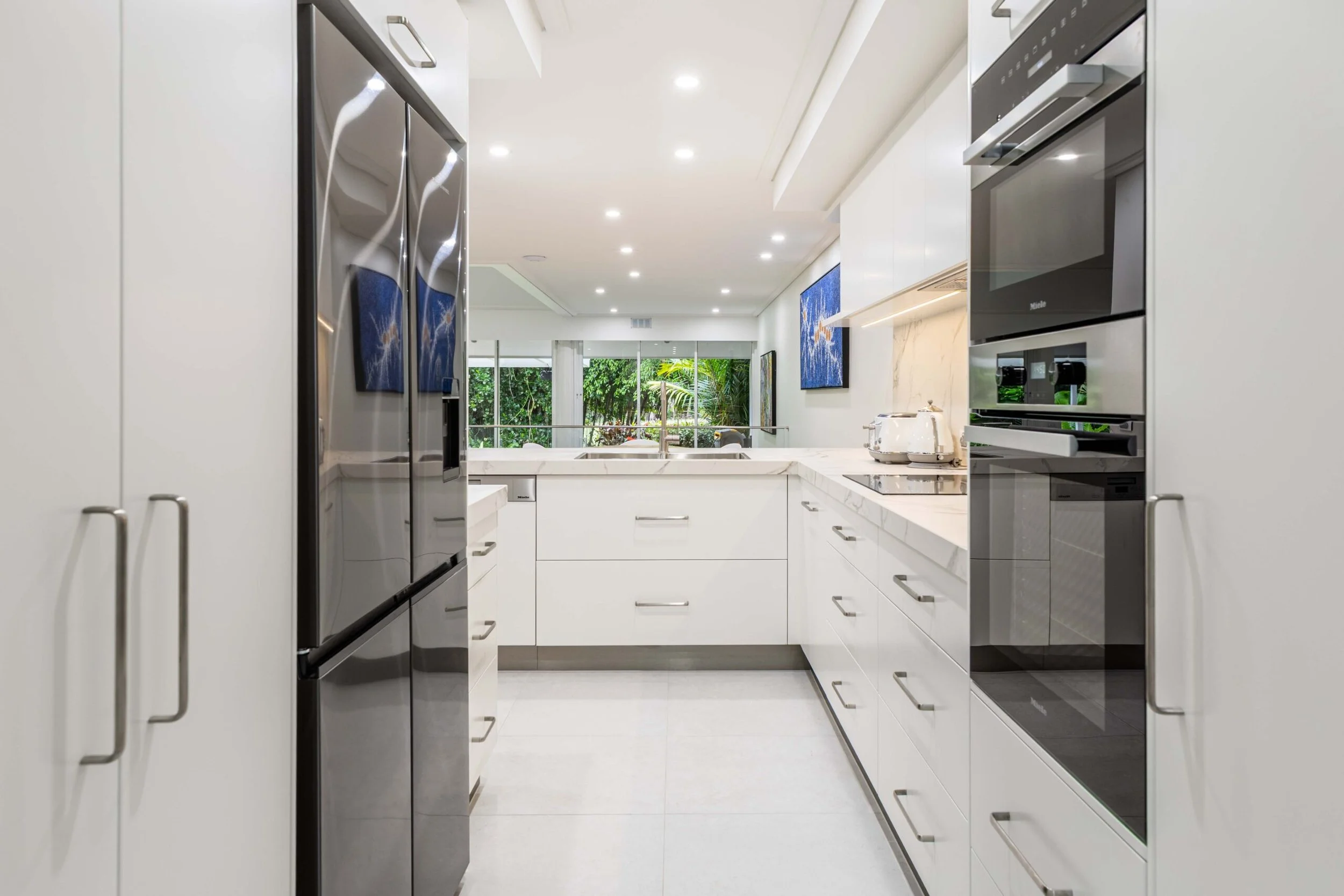 Modern kitchen with white cabinetry, stainless steel appliances, and a window view of green outdoor foliage.