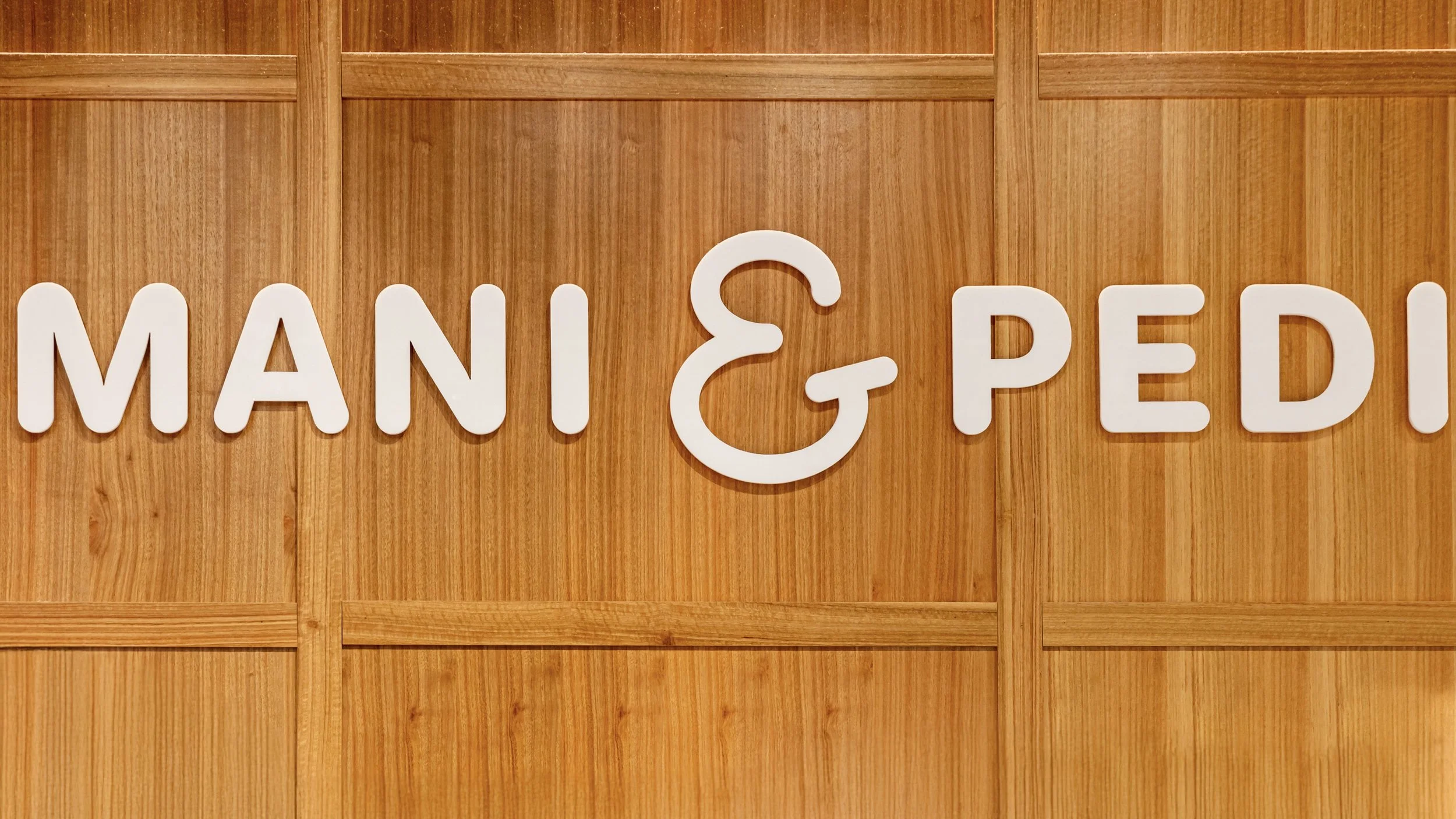 Sign that reads 'MANI & PEDIA' on a wooden wall.