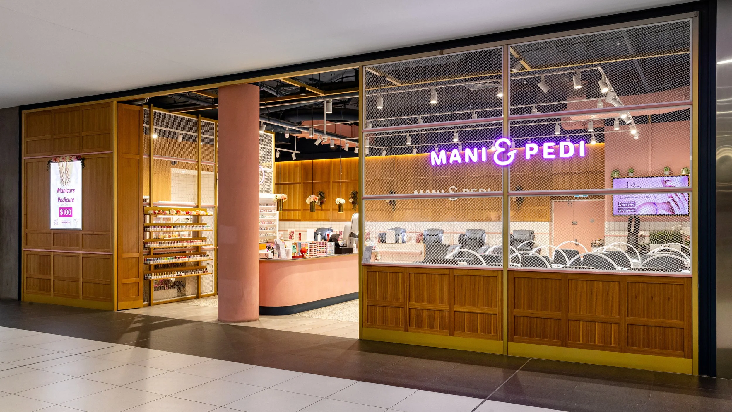 Front view of Mani & Pedi nail salon with pink and wooden decor, illuminated neon sign, manicure and pedicure chairs inside, small display of nail polish bottles, and an information screen outside advertising a manicure pedicure for $100.