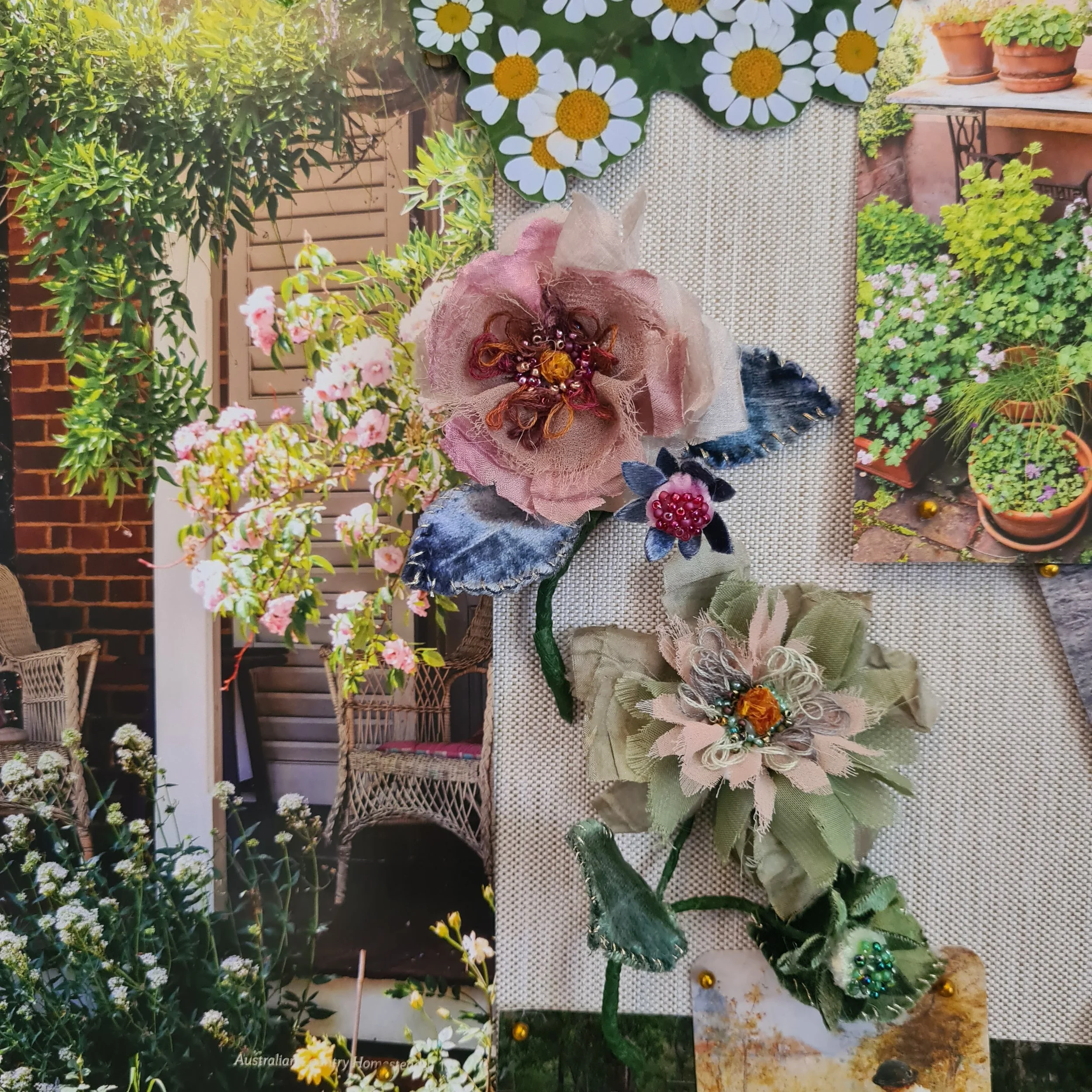 Close-up of artistic mood board showing handmade fabric flower brooches with leaves, set on a textured surface, with a garden background featuring various potted plants and flowers.