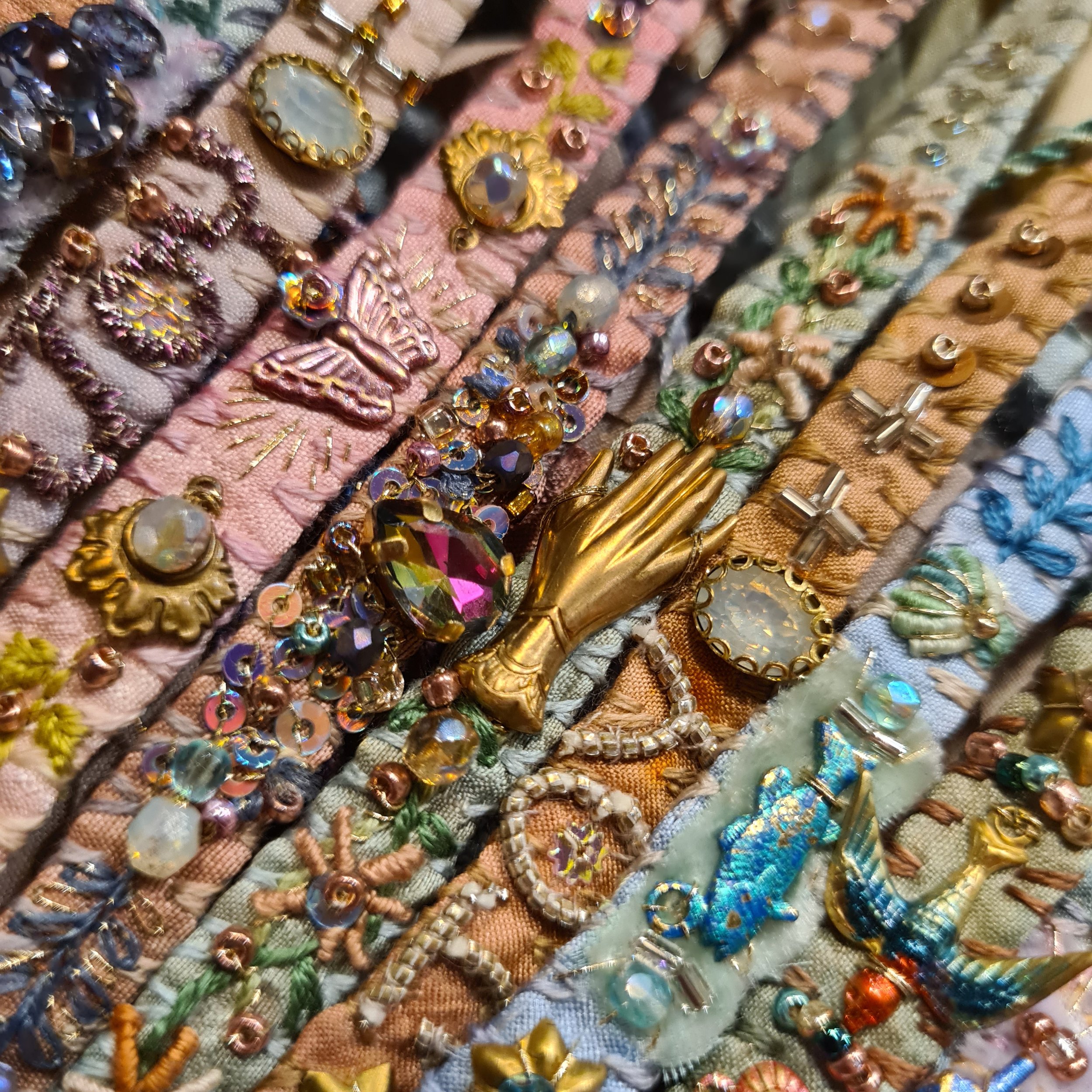 A close-up of colorful embroidered silk bracelets decorated with various charms, beads and embellishments, including rhinestones.