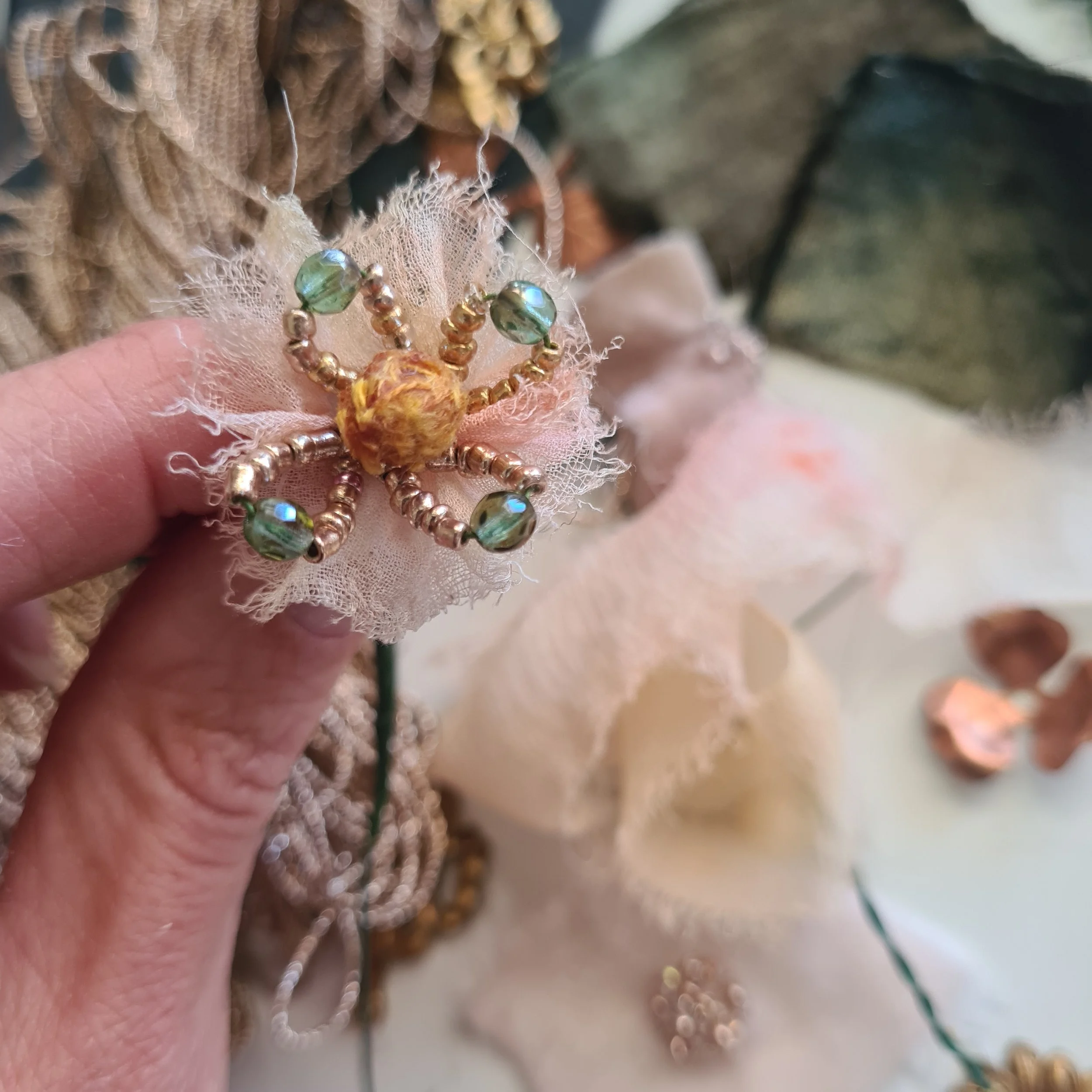 A decorative beaded centre of a flower brooch with a yellow textured stamen and green and gold beads, attached to a pink silk flower.