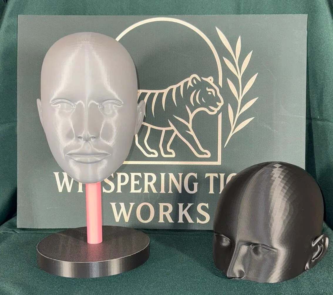 Two mannequin heads, one with a human face mask on a stand and the other as a black head, placed in front of a sign that reads "WTS SPRING TIC WORKS" with a tiger logo.