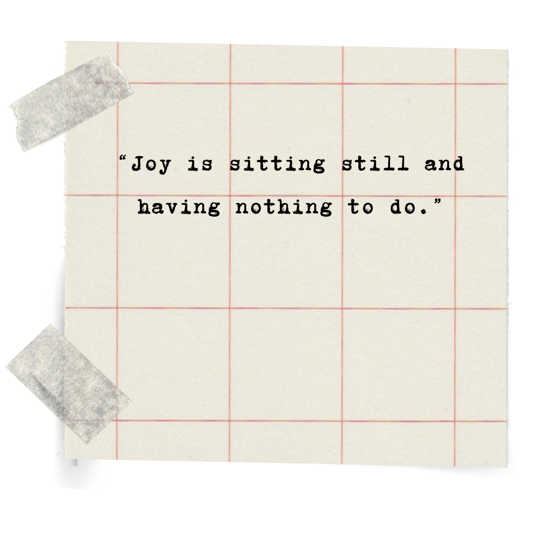 A piece of lined notebook paper with a quote printed on it that reads 'Joy is sitting still and having nothing to do.' The paper has masking tape on the top left and bottom left corners.