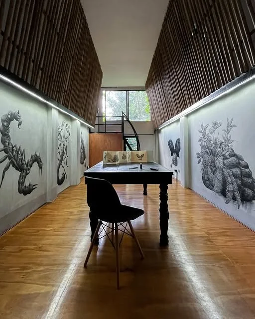 Sala de arte con paredes decoradas con dibujos de animales marinos, un cuadro en la mesa central con mariposas, y una ventana grande al fondo que deja entrar luz natural.