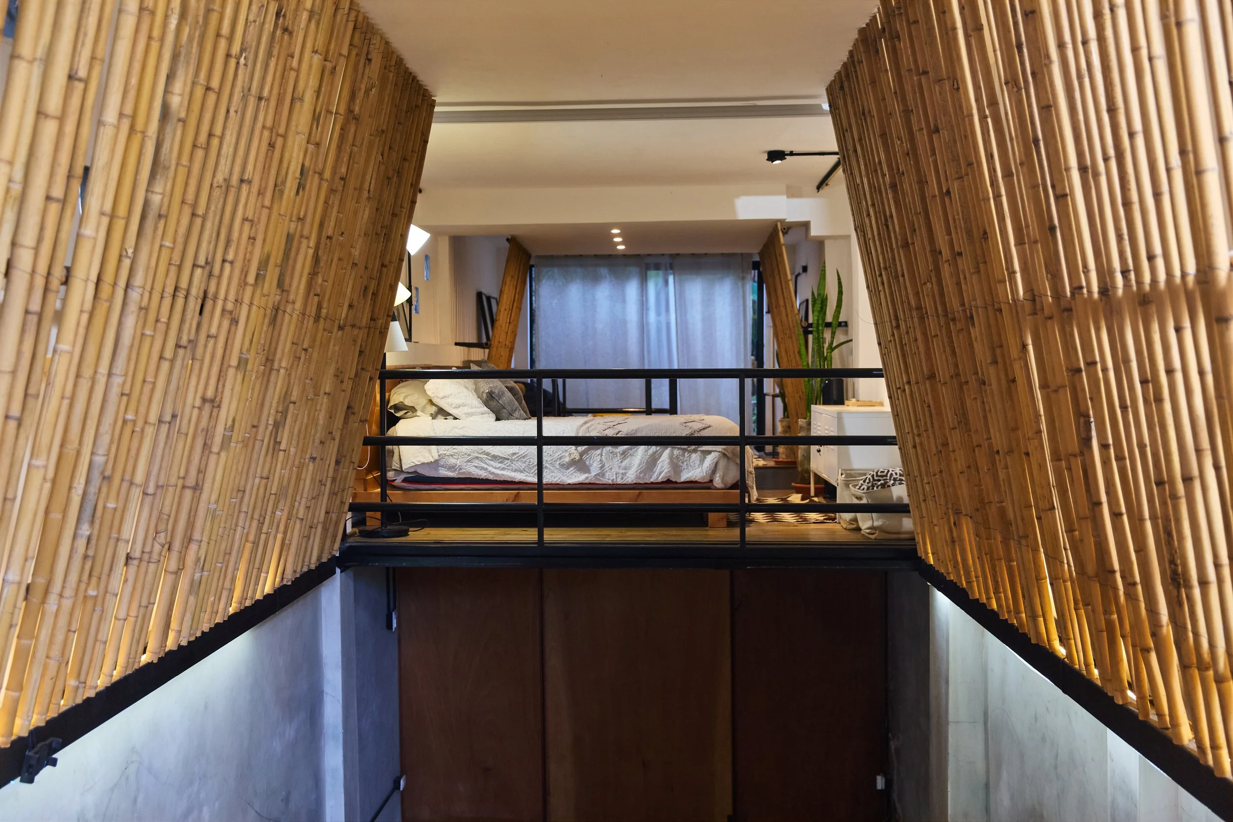 Dormitorio en un apartamento con paredes de caña, camas, cortinas y plantas decorativas.