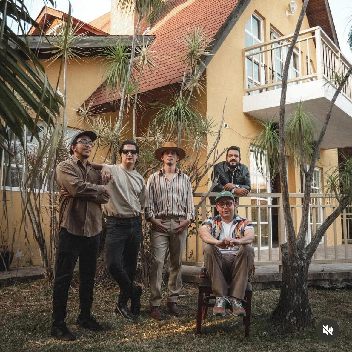 Grupo de cinco personas posando en un jardín frente a una casa de dos pisos, con árboles y plantas tropicales.