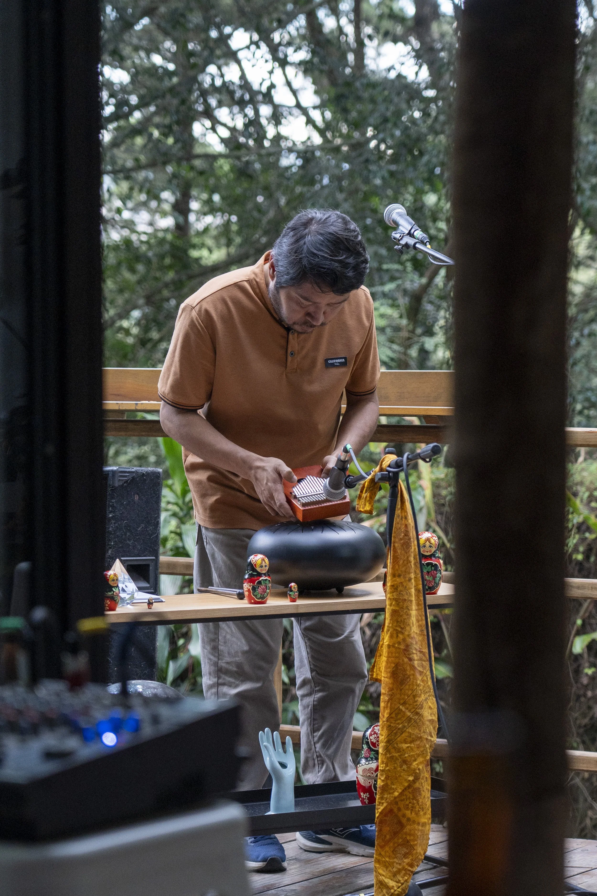 Un hombre en un entorno natural ajustando un instrumento musical en una mesa con tazas rusas y otros objetos decorativos.