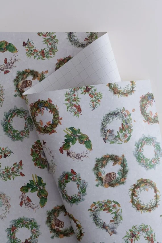 Holiday-themed wrapping paper with Christmas wreath designs featuring owls, pinecones, holly, and other festive elements.