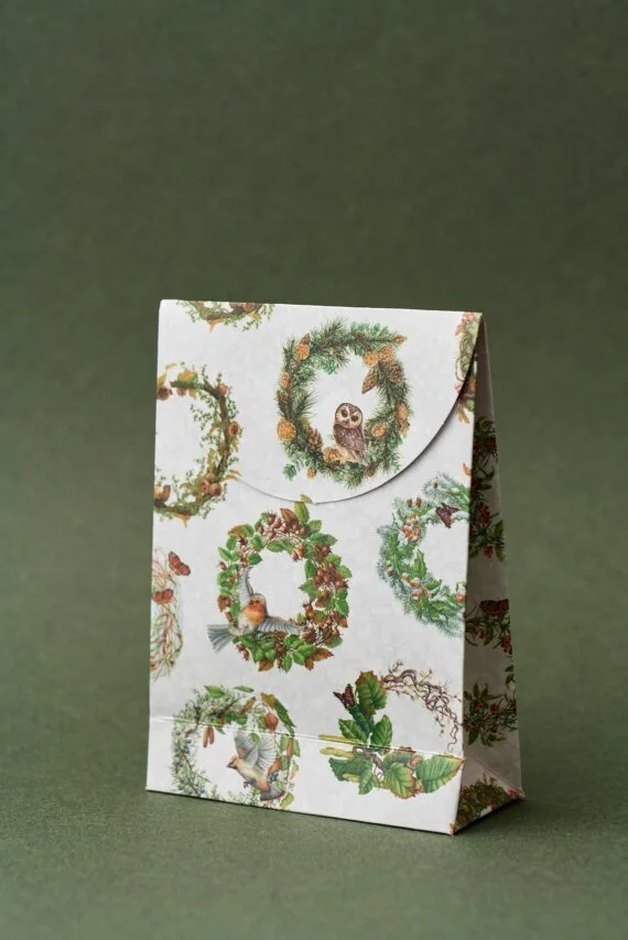 A festive paper gift bag with holiday wreath designs and an owl illustration on a green background.