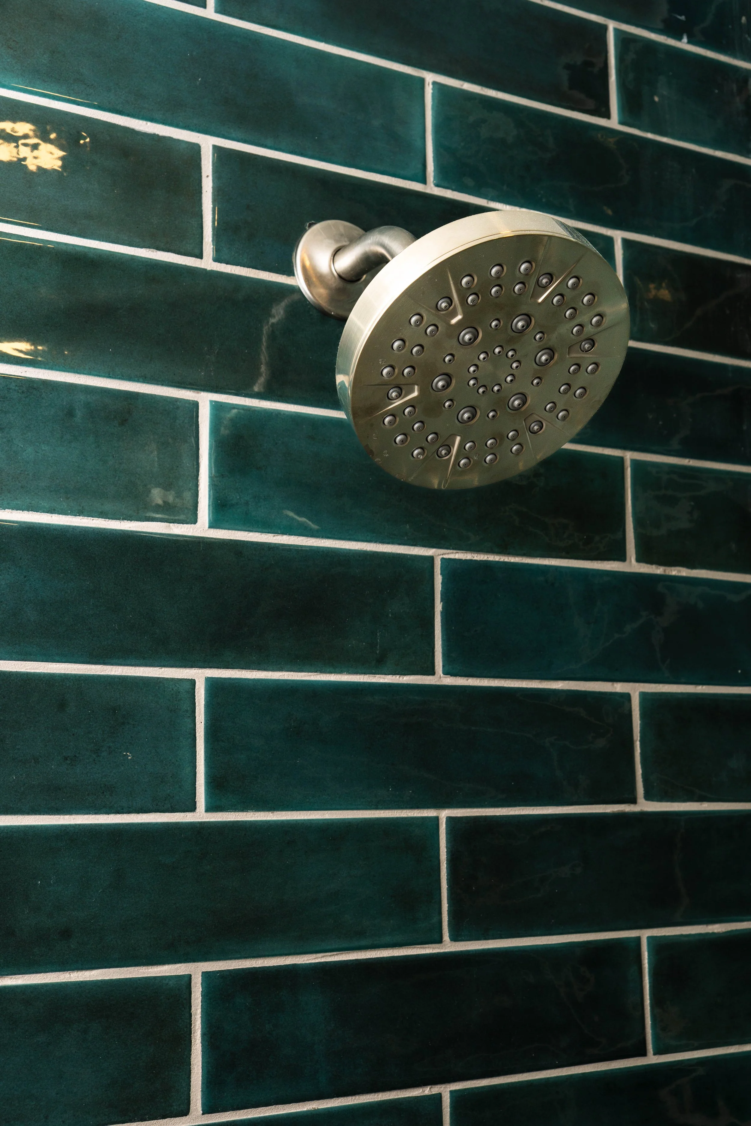 A metallic showerhead mounted on a green tiled bathroom wall.