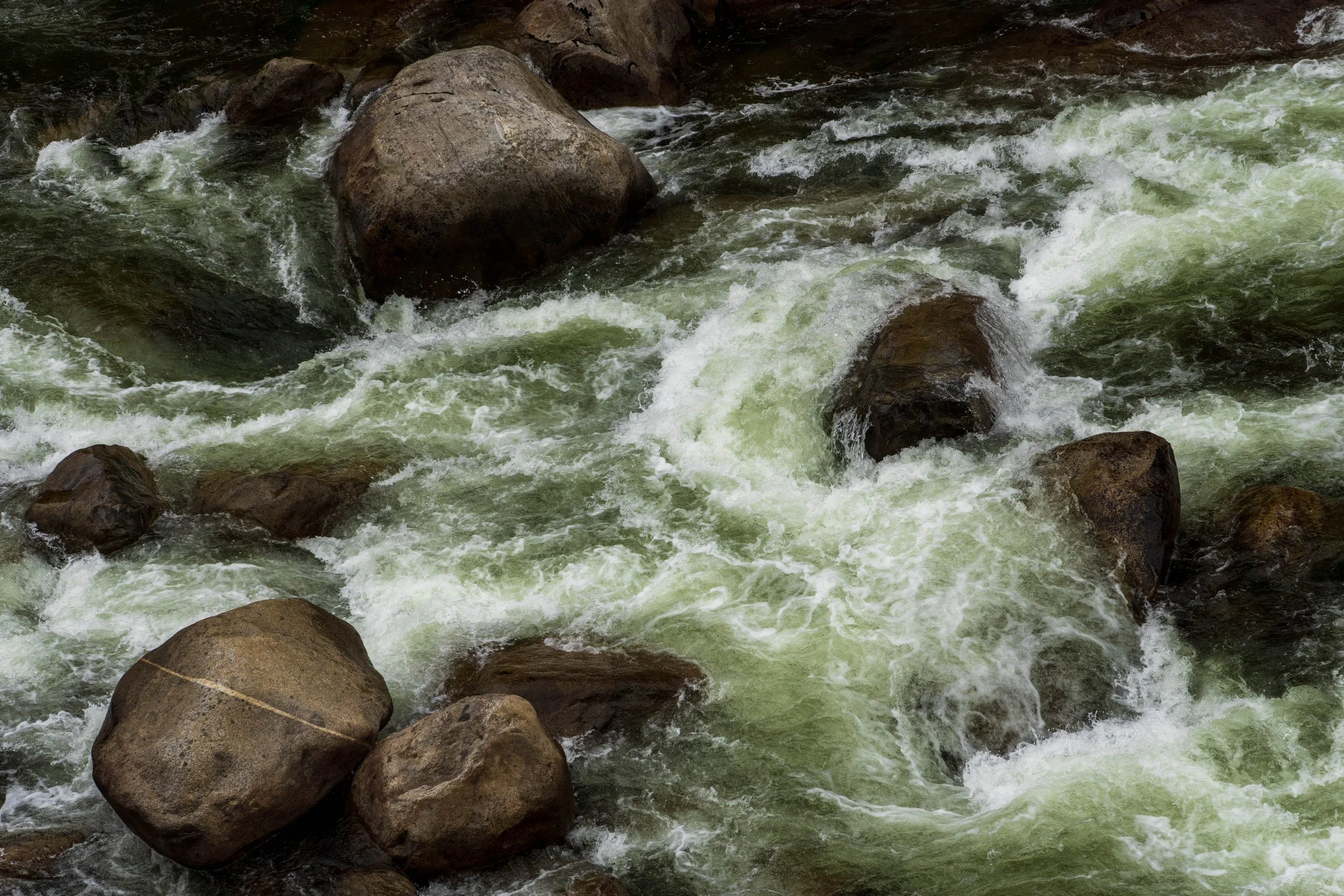 Flowing river water around large rocks in a natural setting.