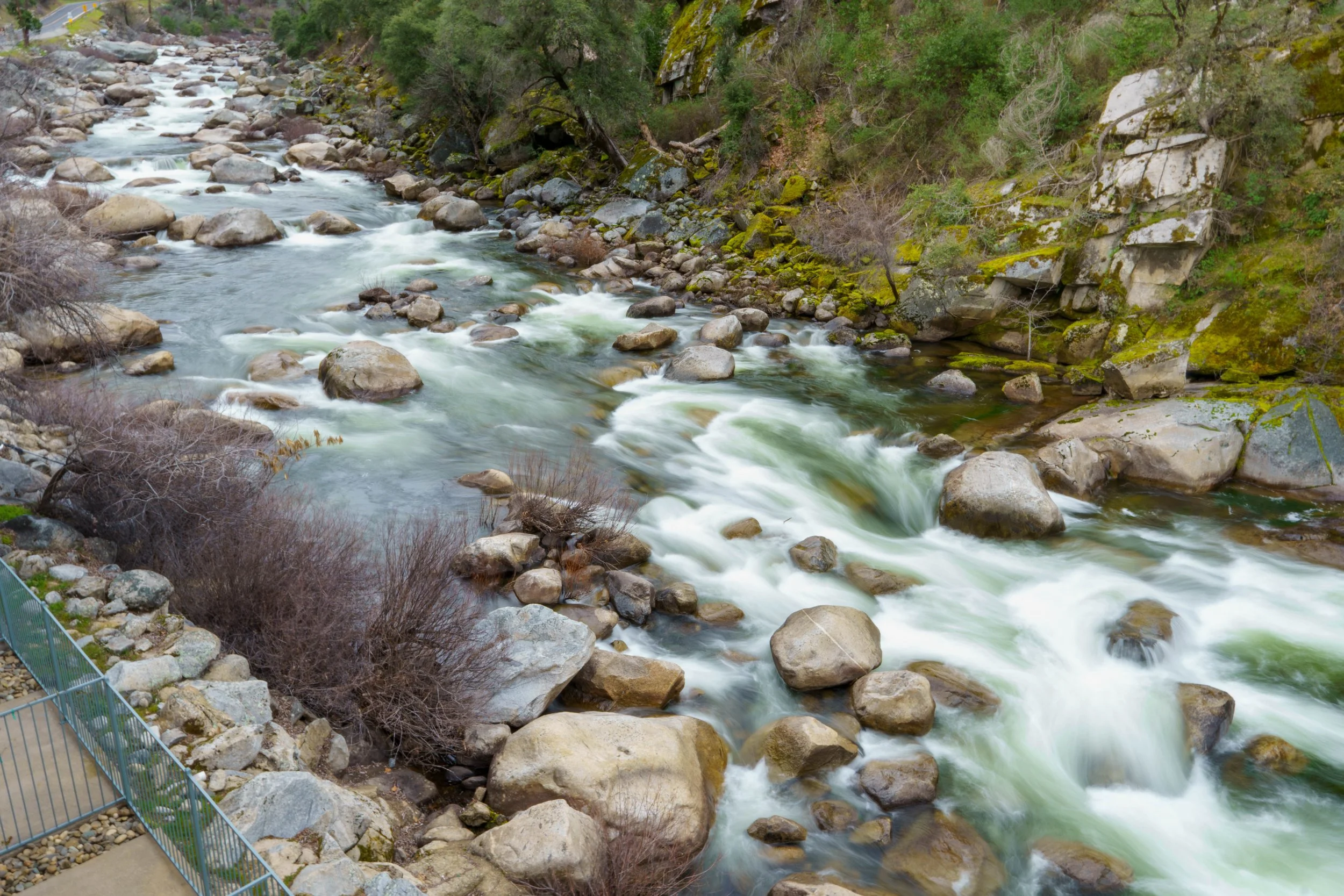 A flowing river with rocks surrounded by trees and moss-covered rocks on a hillside.