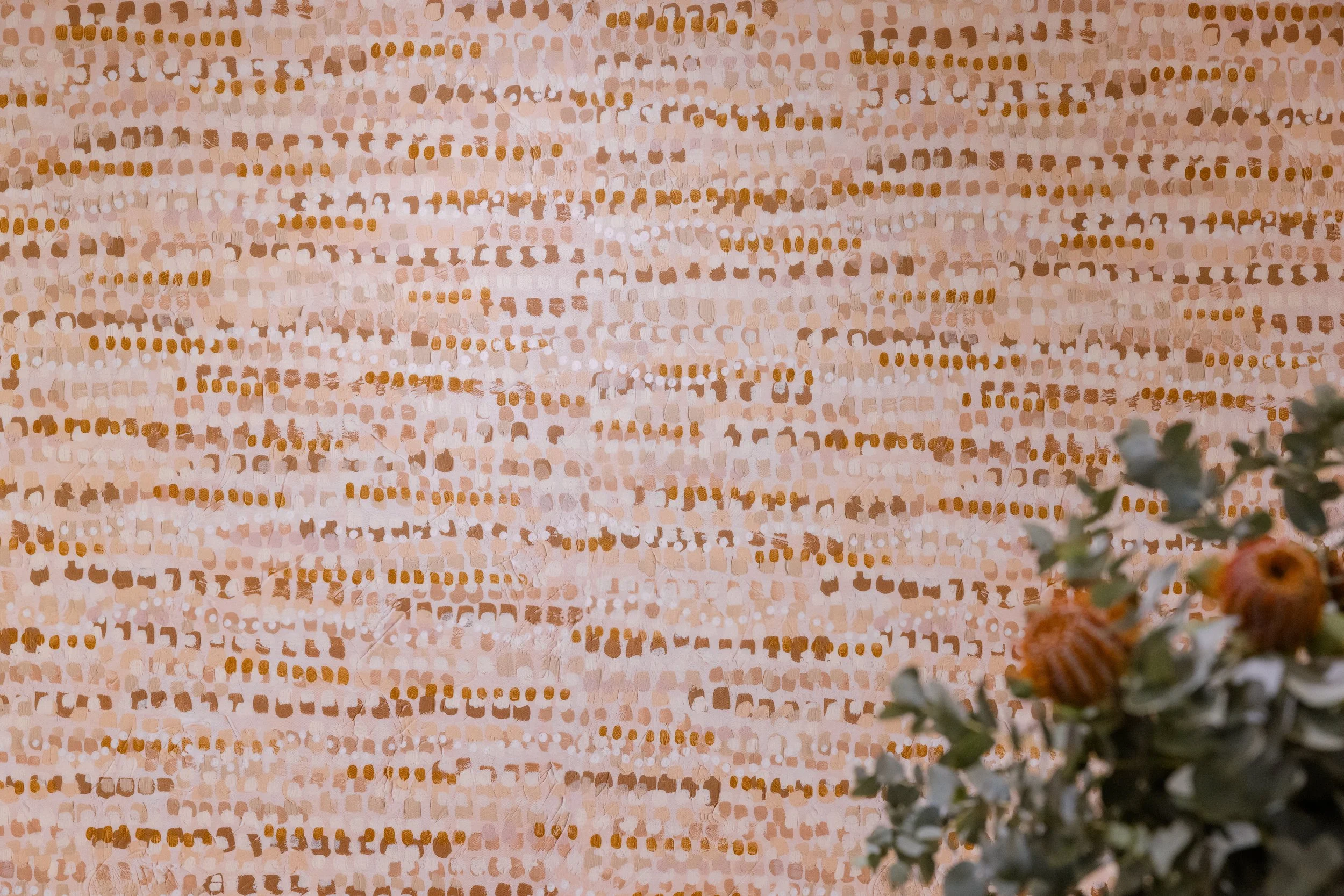 A textured wall with a pattern of small, irregular, ochre and beige squares and rectangles, with greenery and orange flowers in the bottom right corner.