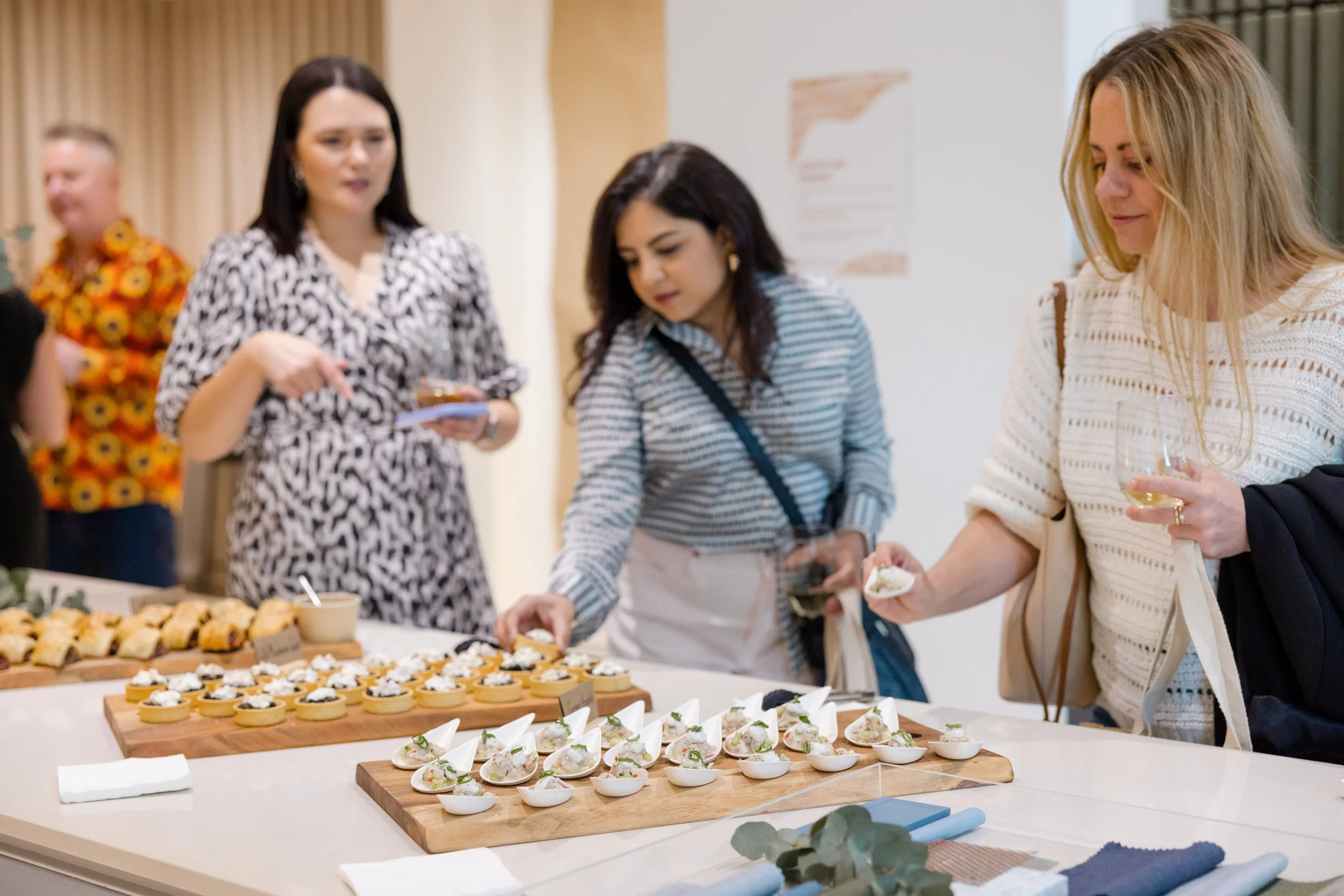 People serving themselves small bites and drinks at a food table during a social gathering.