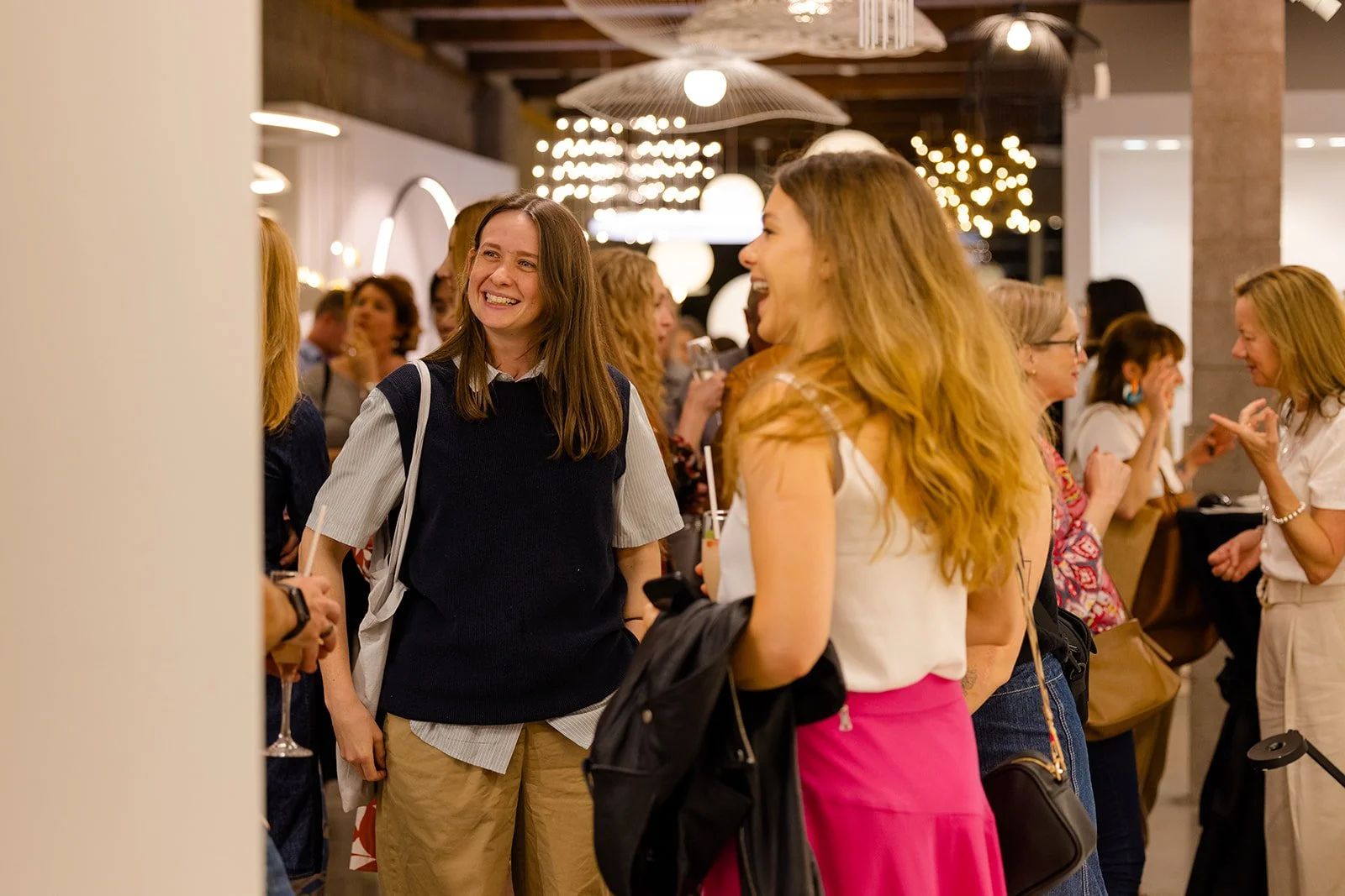 People socializing and smiling at an indoor gathering or event with decorative lighting.